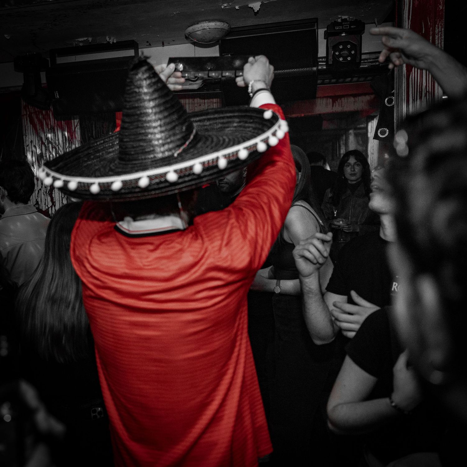Person iført en festlig sombrero med pomponer danser i en rød skjorte foran en sort-hvid baggrund.