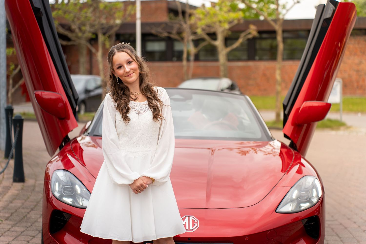 A white dress contrasts beautifully with a red Tesla Model 3 with butterfly doors open on each side.