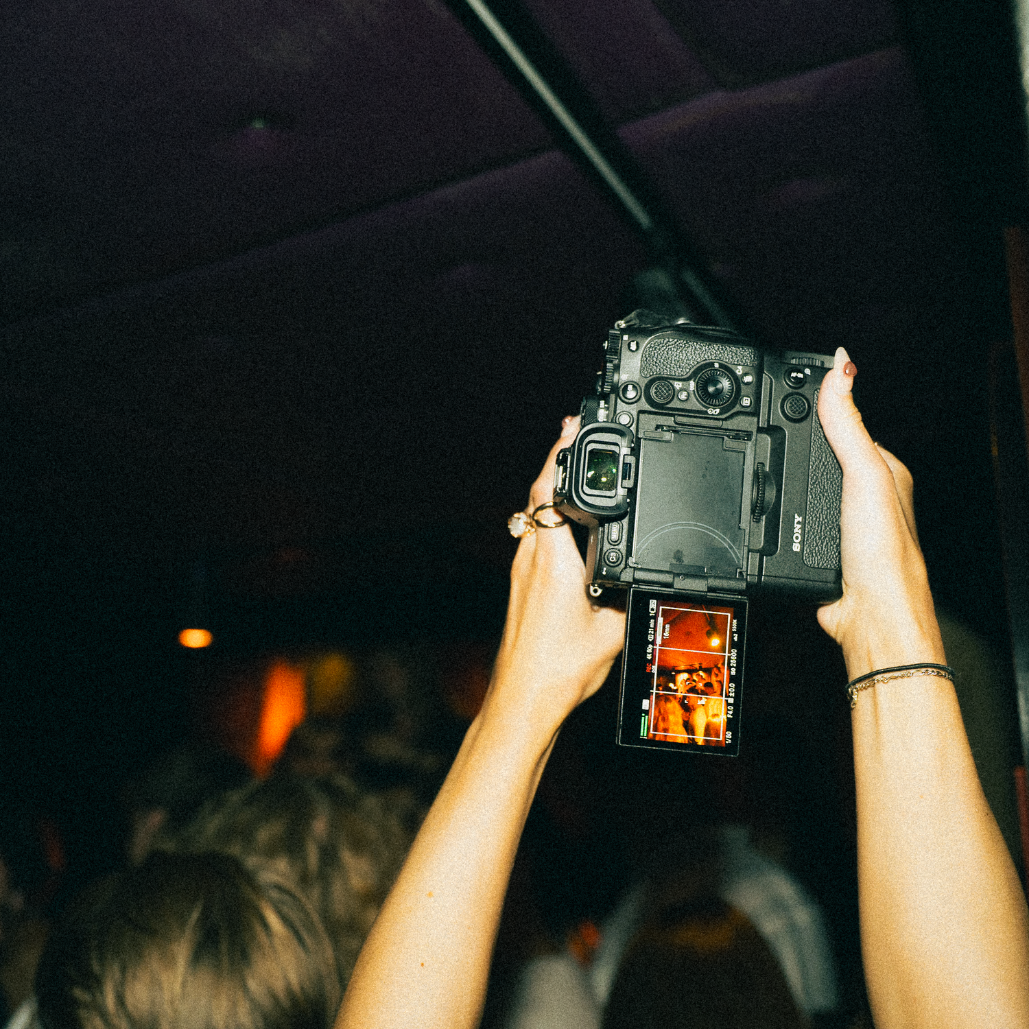 Hands holding up a DSLR camera at a concert venue to capture photos in low light conditions.