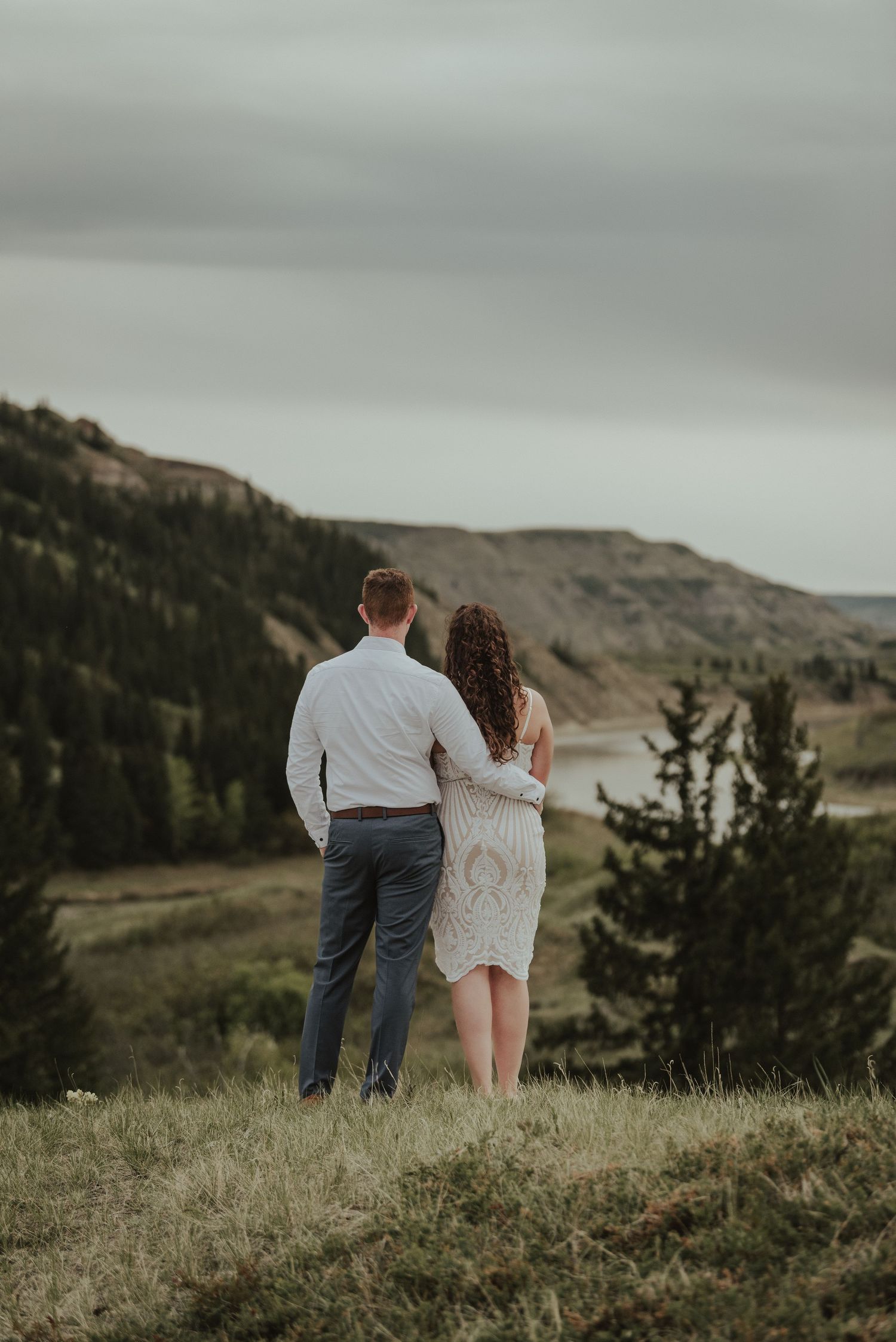 Couple standing together on hilltop overlooking scenic mountain valley and winding river.
