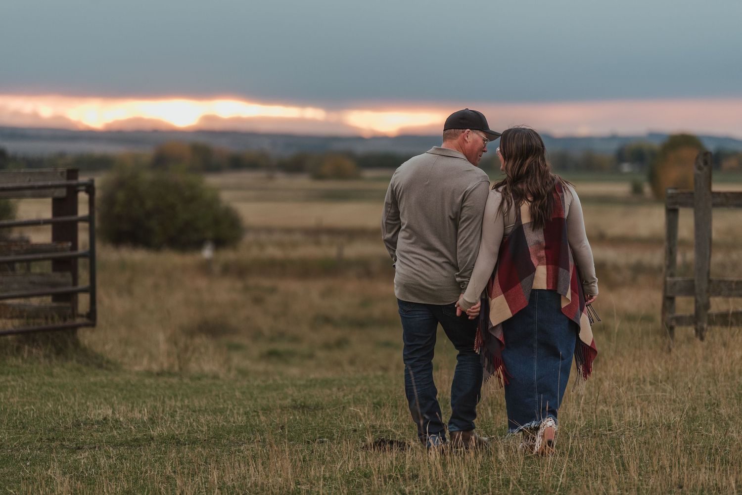 Intimate couple sharing moment at sunset in rural farm field with wooden gate.