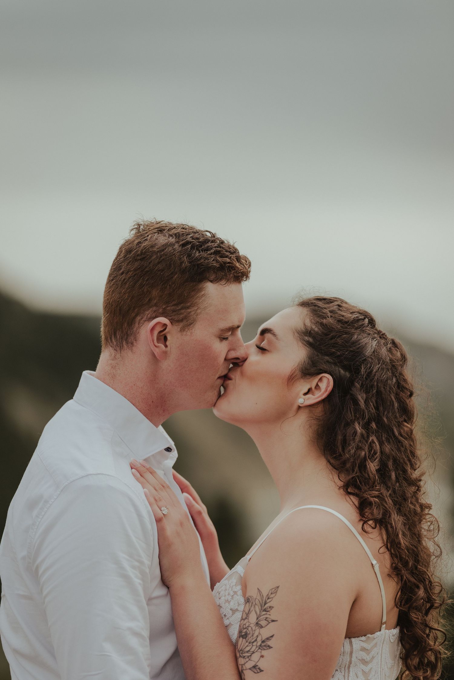 Intimate moment between couple sharing romantic kiss against mountain backdrop.