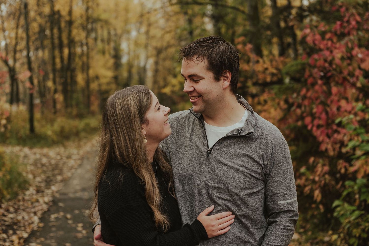 Couple sharing loving glances on autumn path surrounded by colorful fall foliage.
