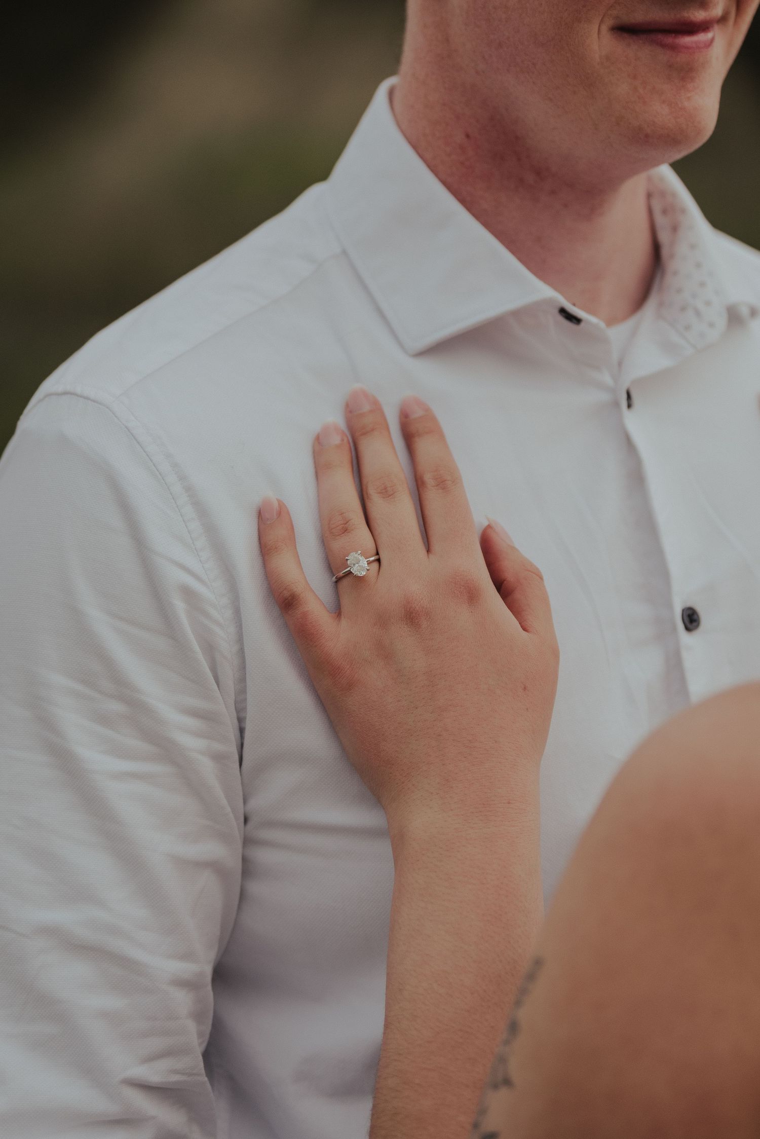Close up of engagement ring displayed on hand against white shirt.