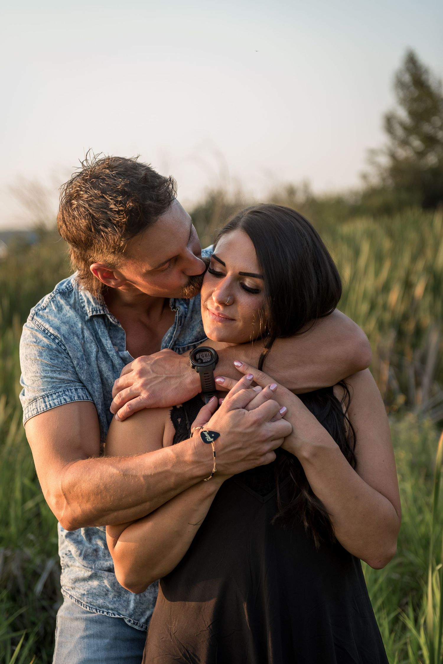Intimate moment between a couple hugging in tall summer grass at sunset.