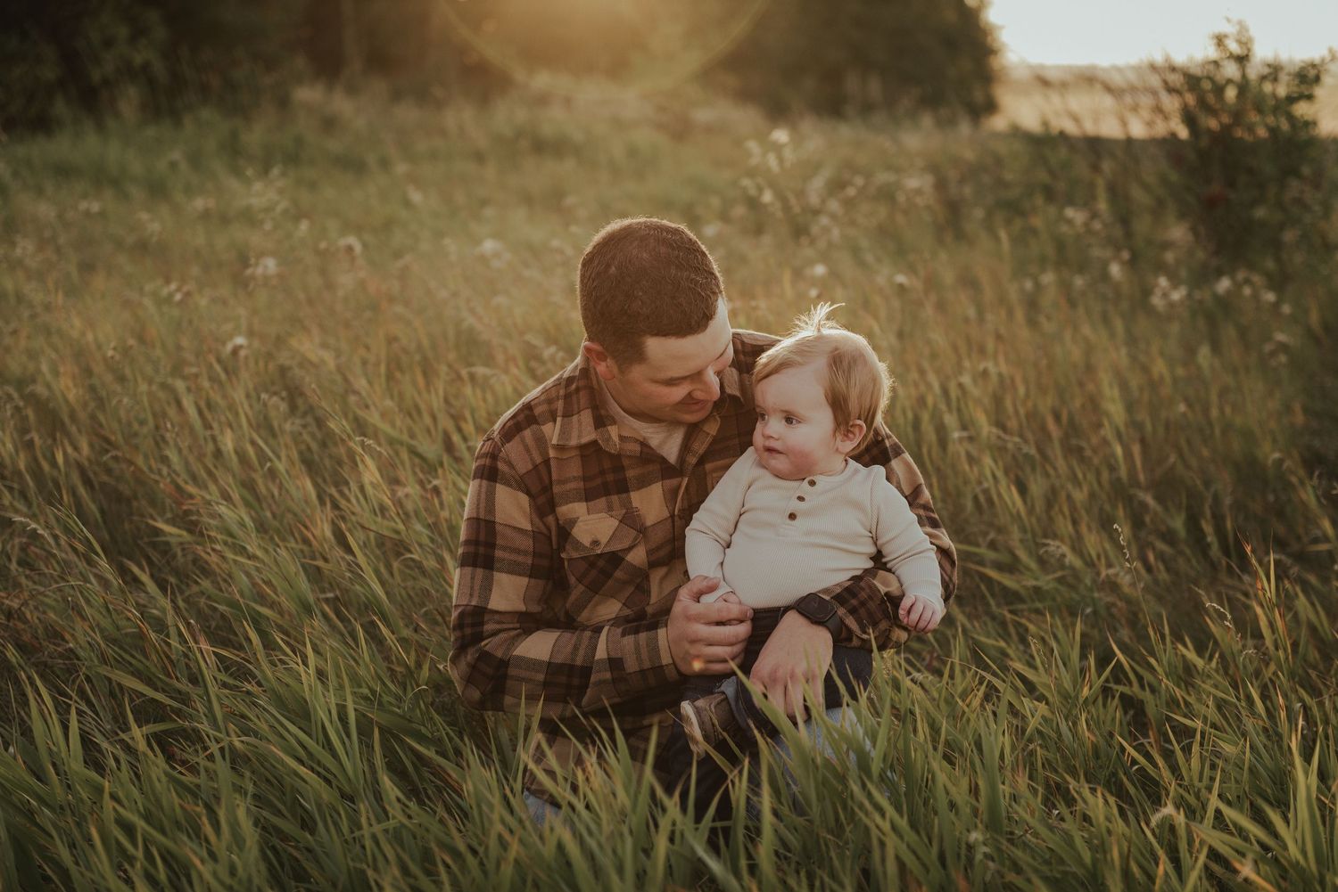 Parent and baby sharing tender moment in golden sunset field.