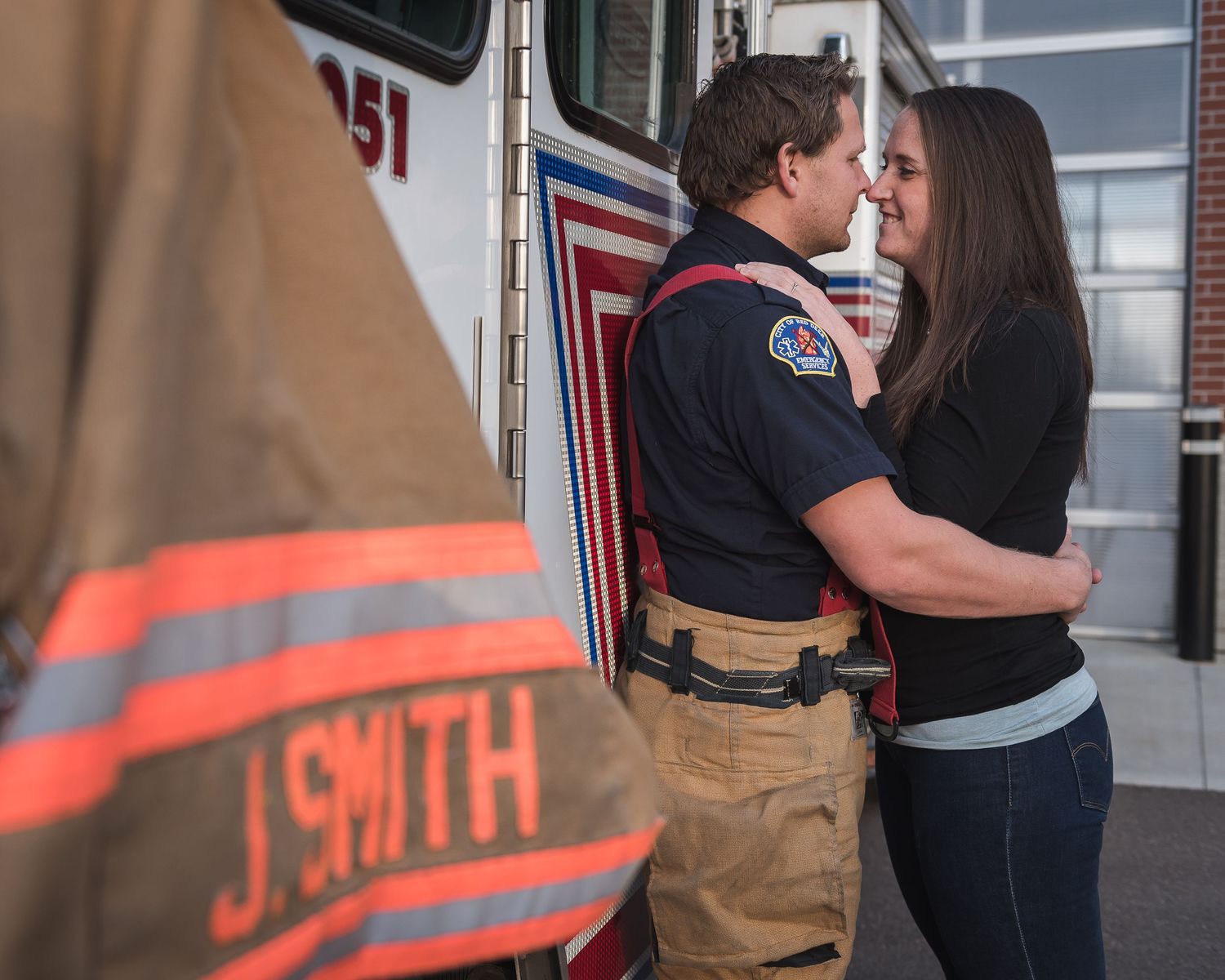 A firefighter in uniform shares an intimate moment with someone near an emergency vehicle.