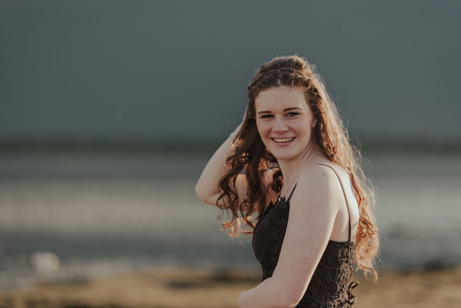 A person poses in a dark dress amidst tall grass during golden hour.