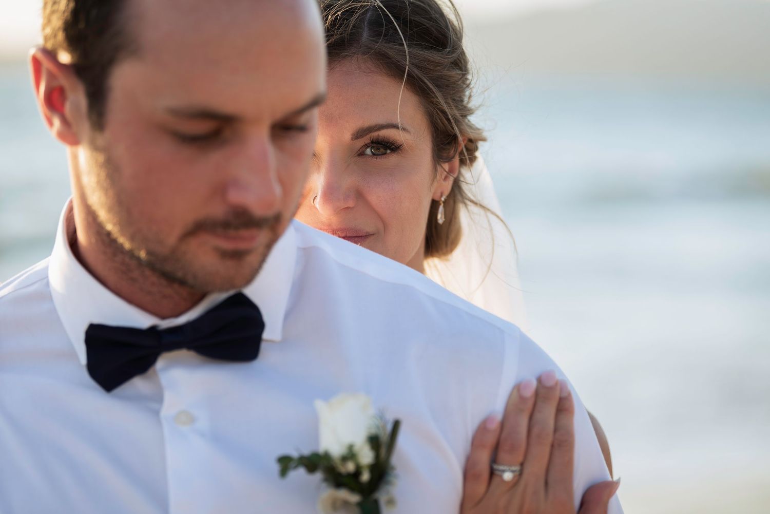 Close up portrait of a romantic couple on the beach at wedding with white tuxedo and black bow tie.