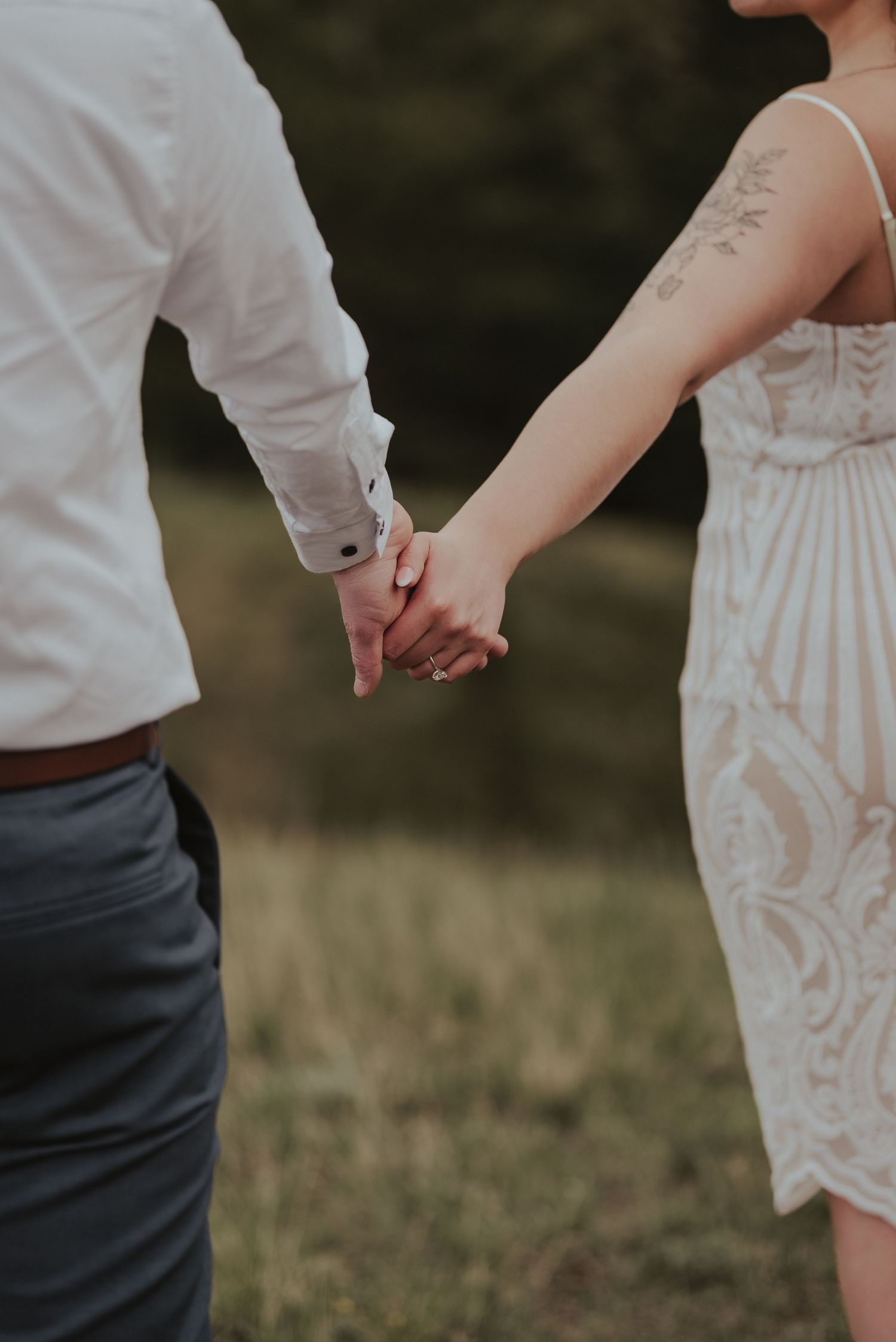 Close up of couple holding hands showing delicate lace dress detail and visible tattoo.