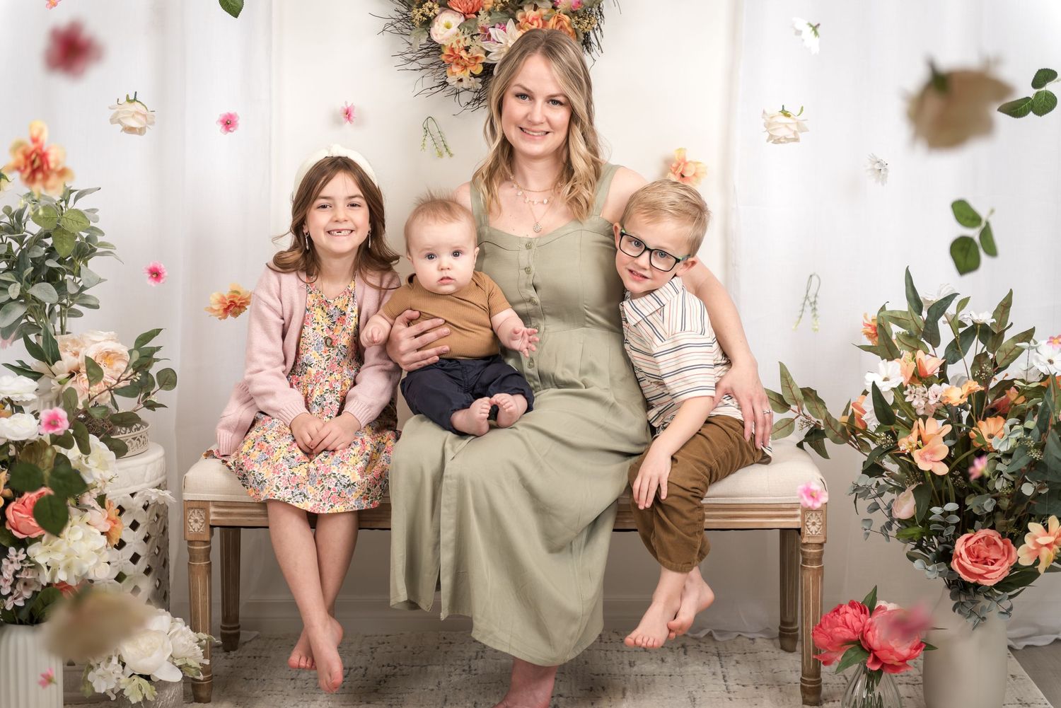 A spring family portrait with floral decorations and a rustic bench against a white backdrop.