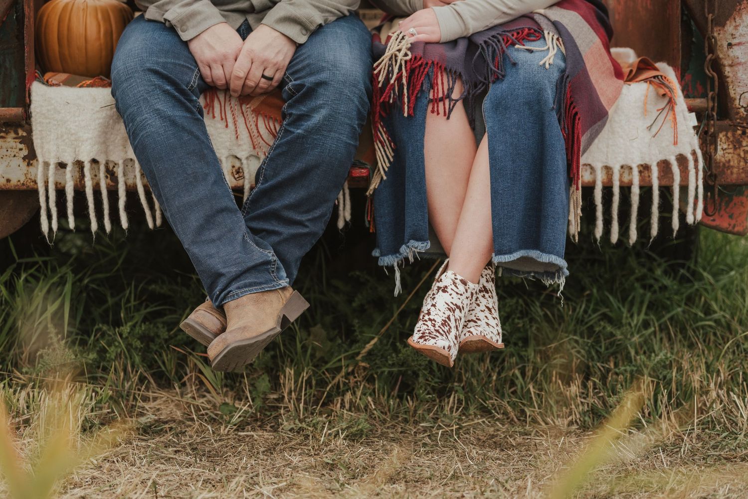 Close-up of two pairs of legs sitting on a rustic bench with pumpkins in background.