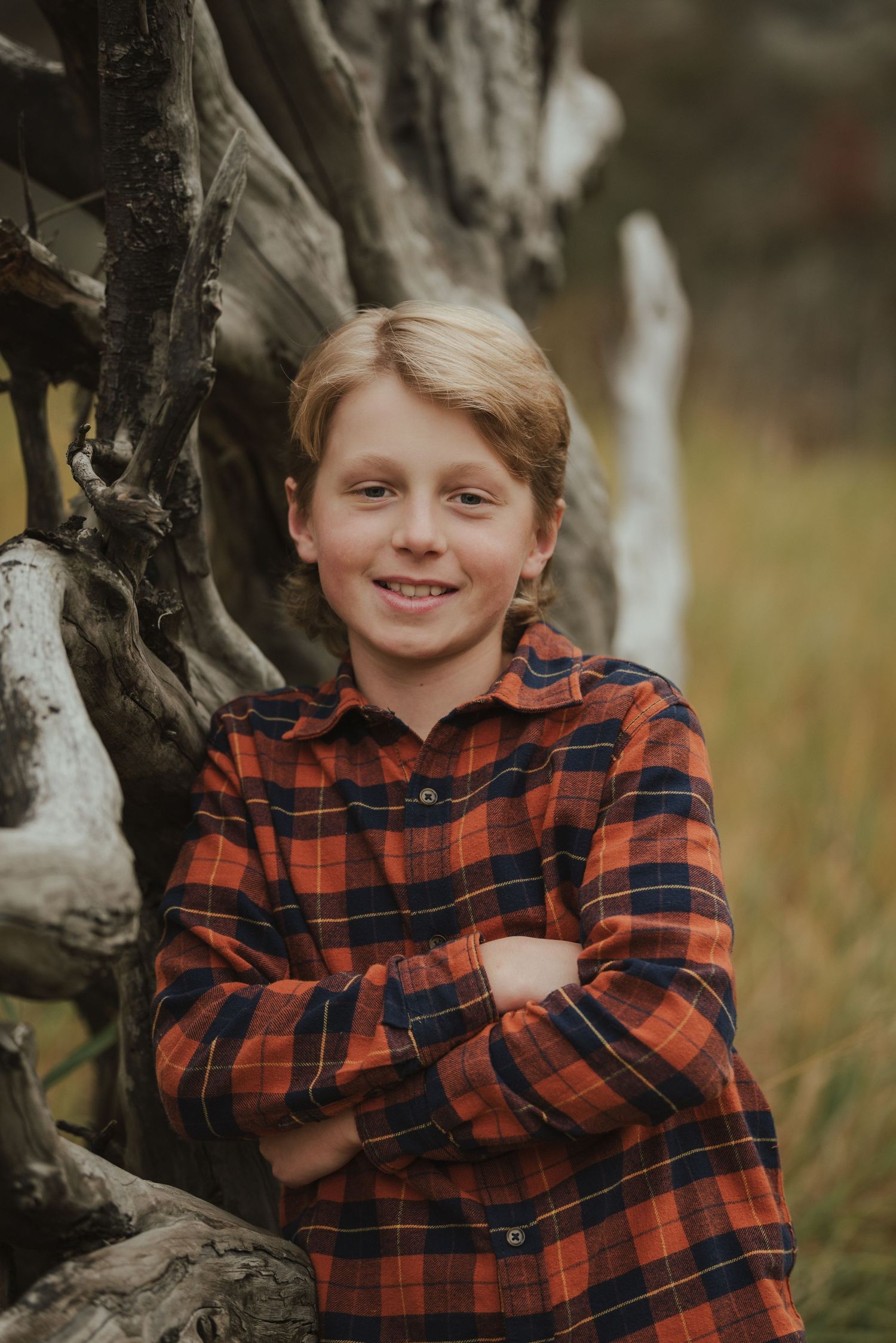 A youth in a red plaid flannel shirt poses confidently against a weathered wooden backdrop.