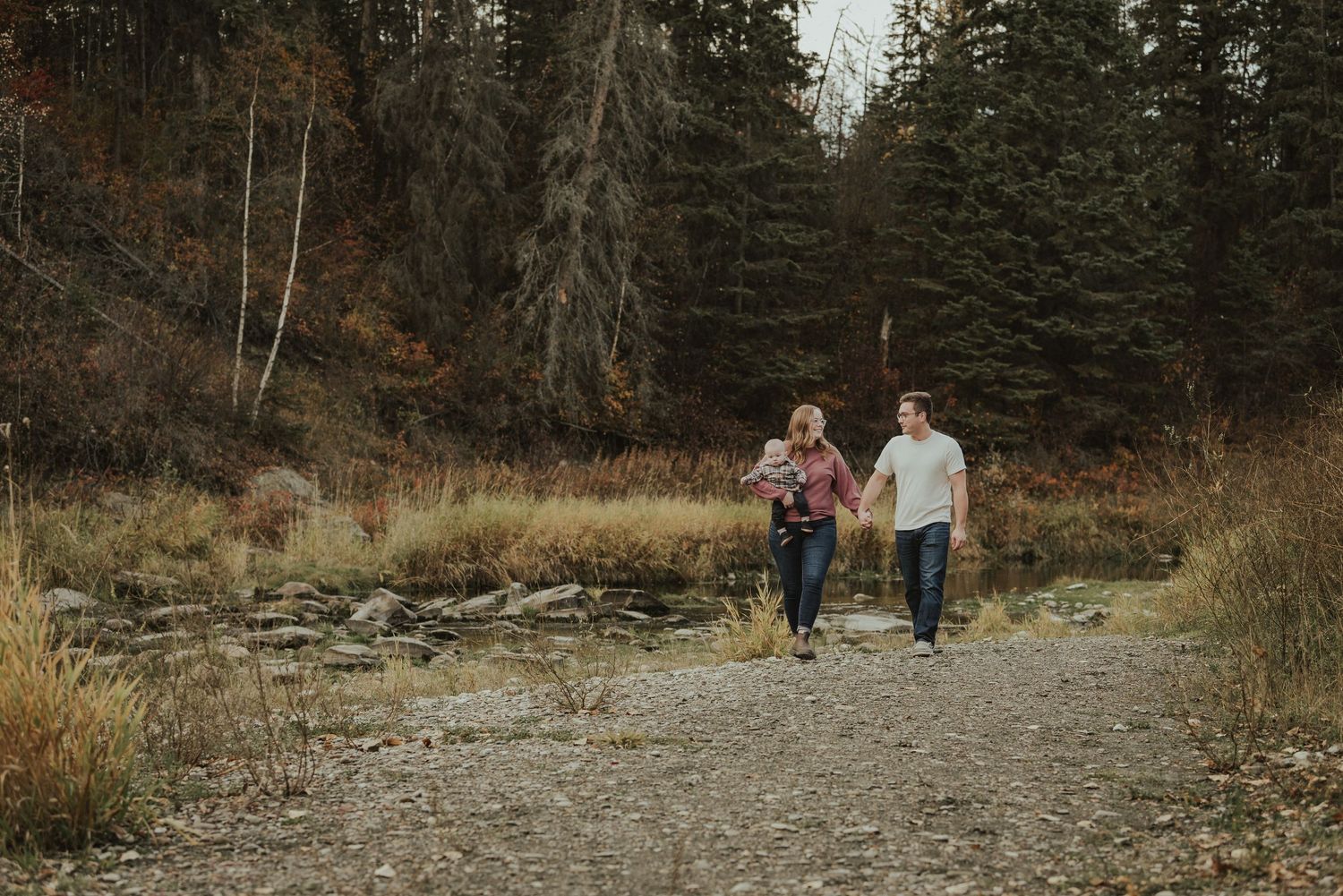 Couple walking hand in hand on gravel path through autumn mountain landscape.