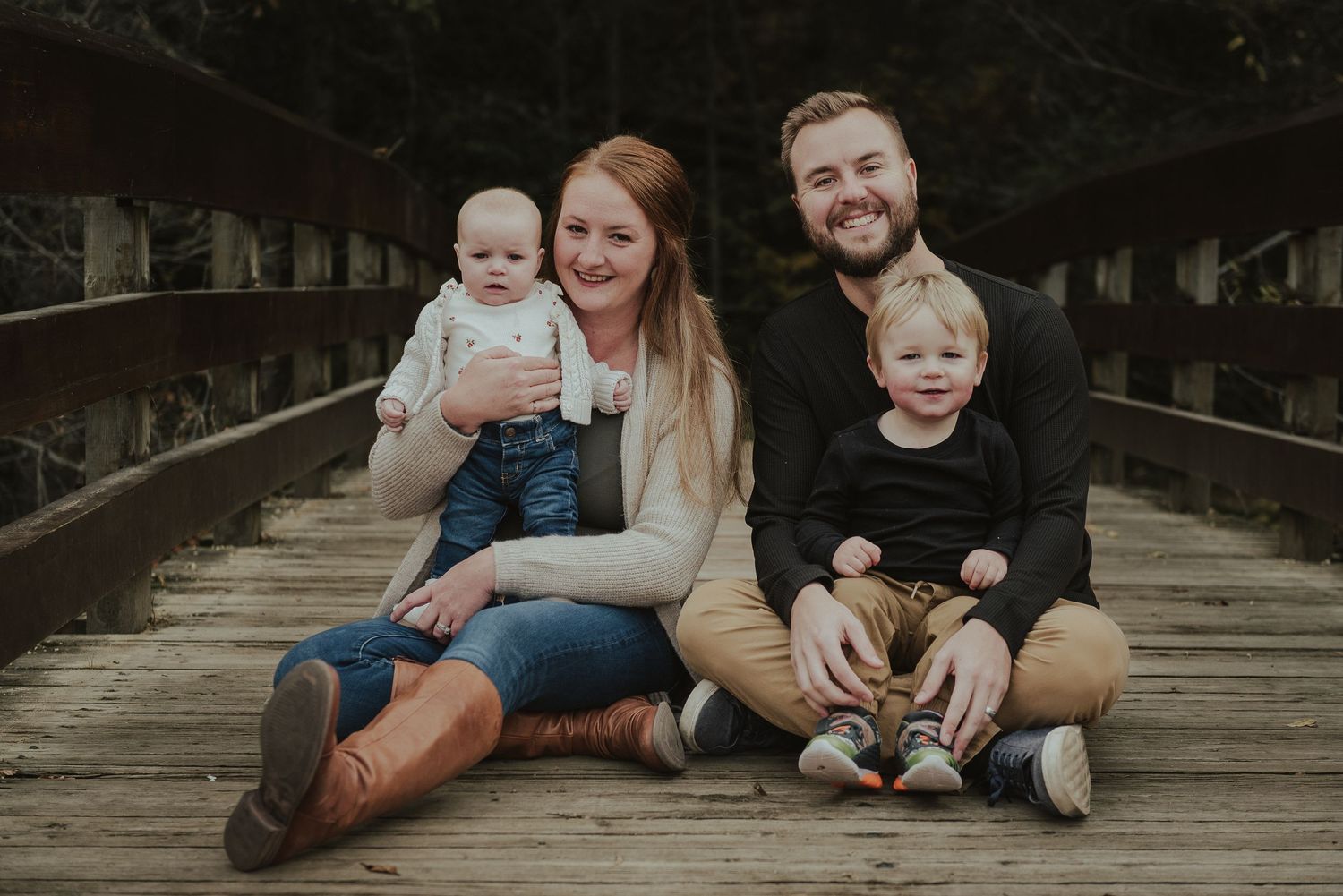 A young family poses together on a wooden bridge for a portrait.