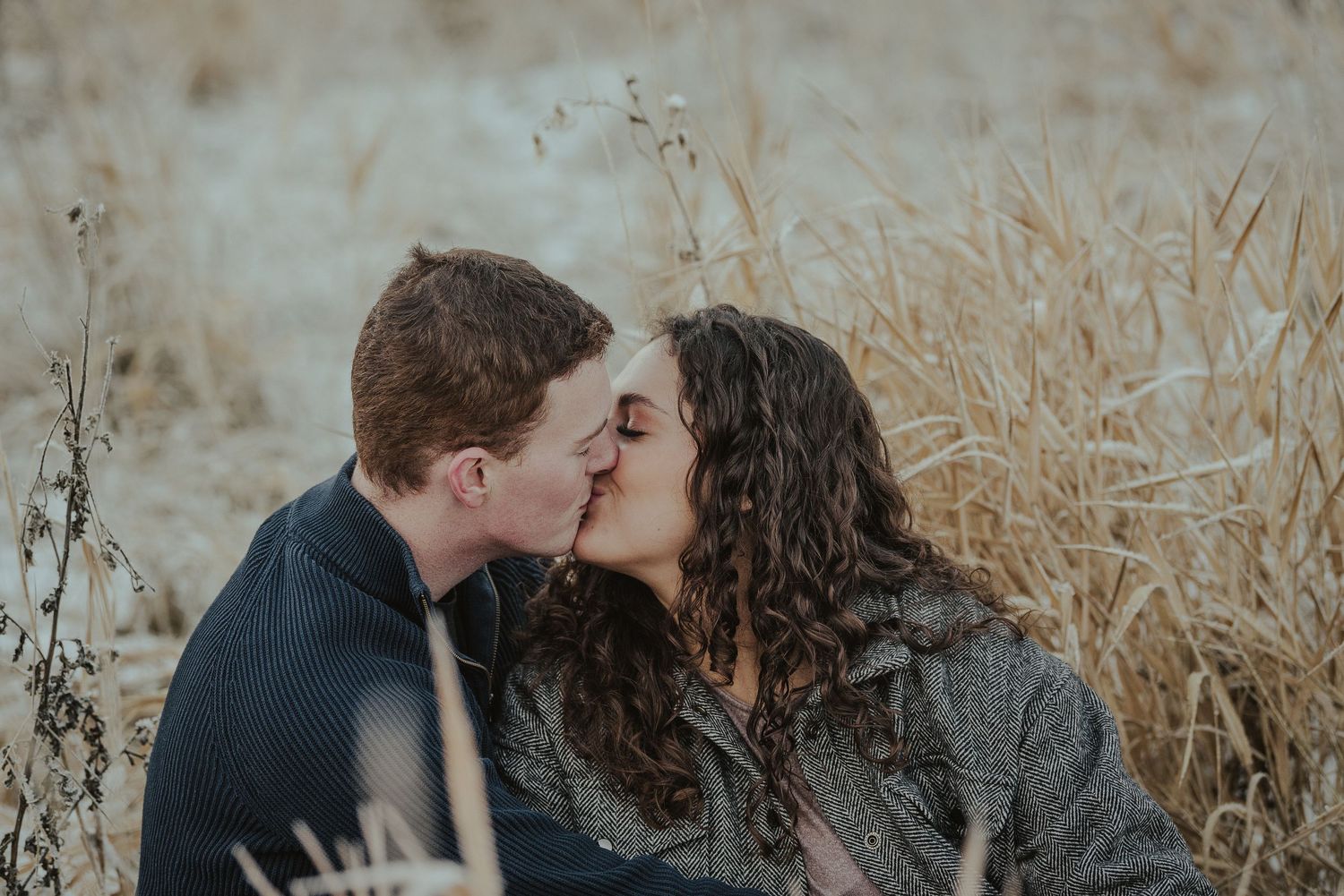 Close romantic moment between couple in dark sweaters among tall dry grass.