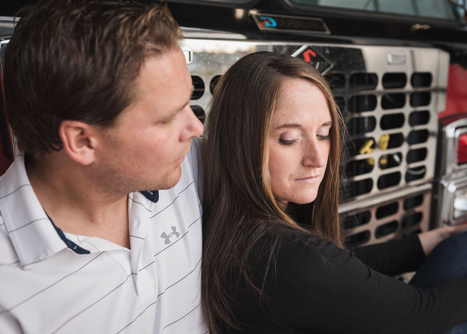 Intimate portrait of a couple sitting close together on a fire truck during their engagement session.
