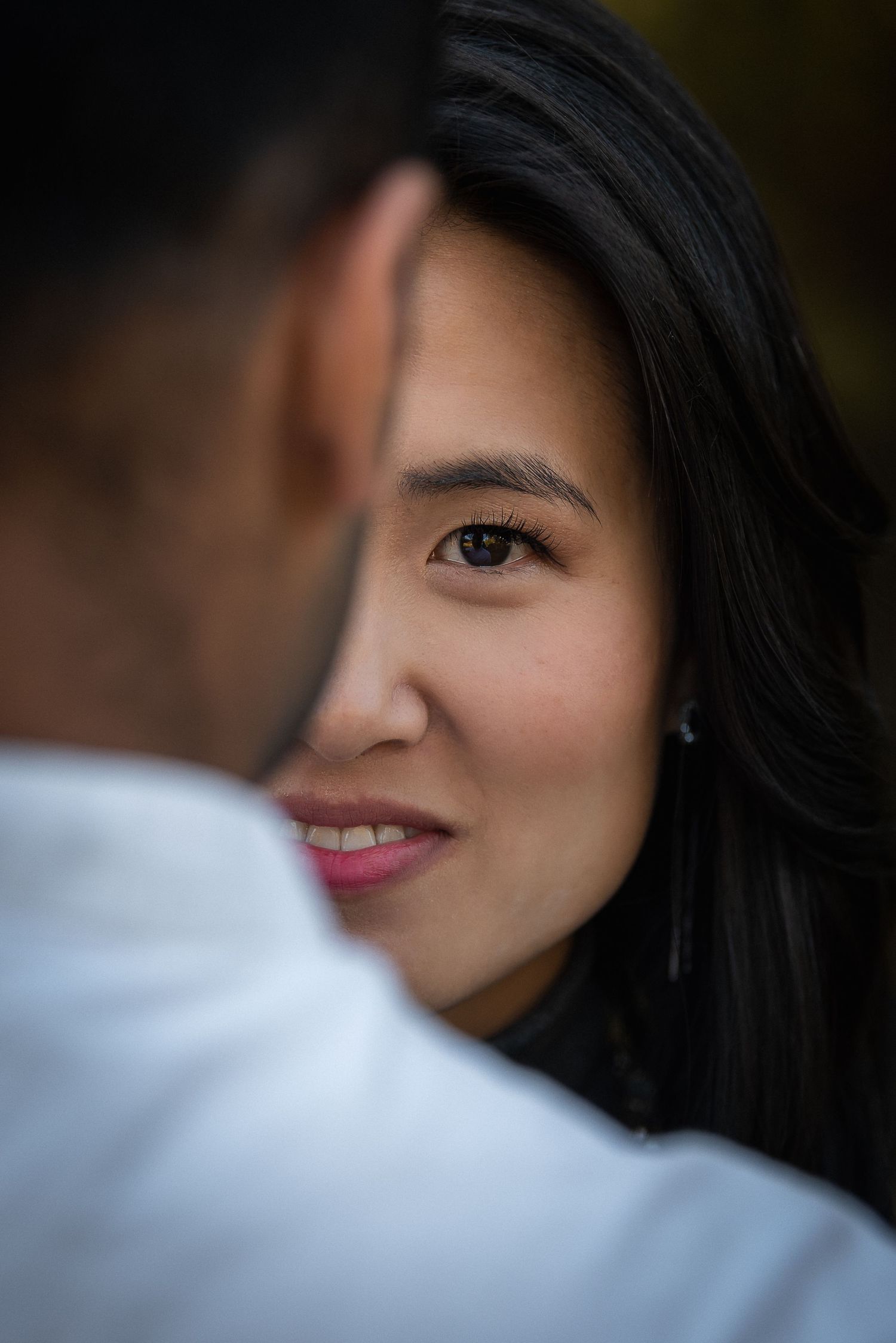Close up portrait showing half of a smiling face with dark hair against a blurred background.