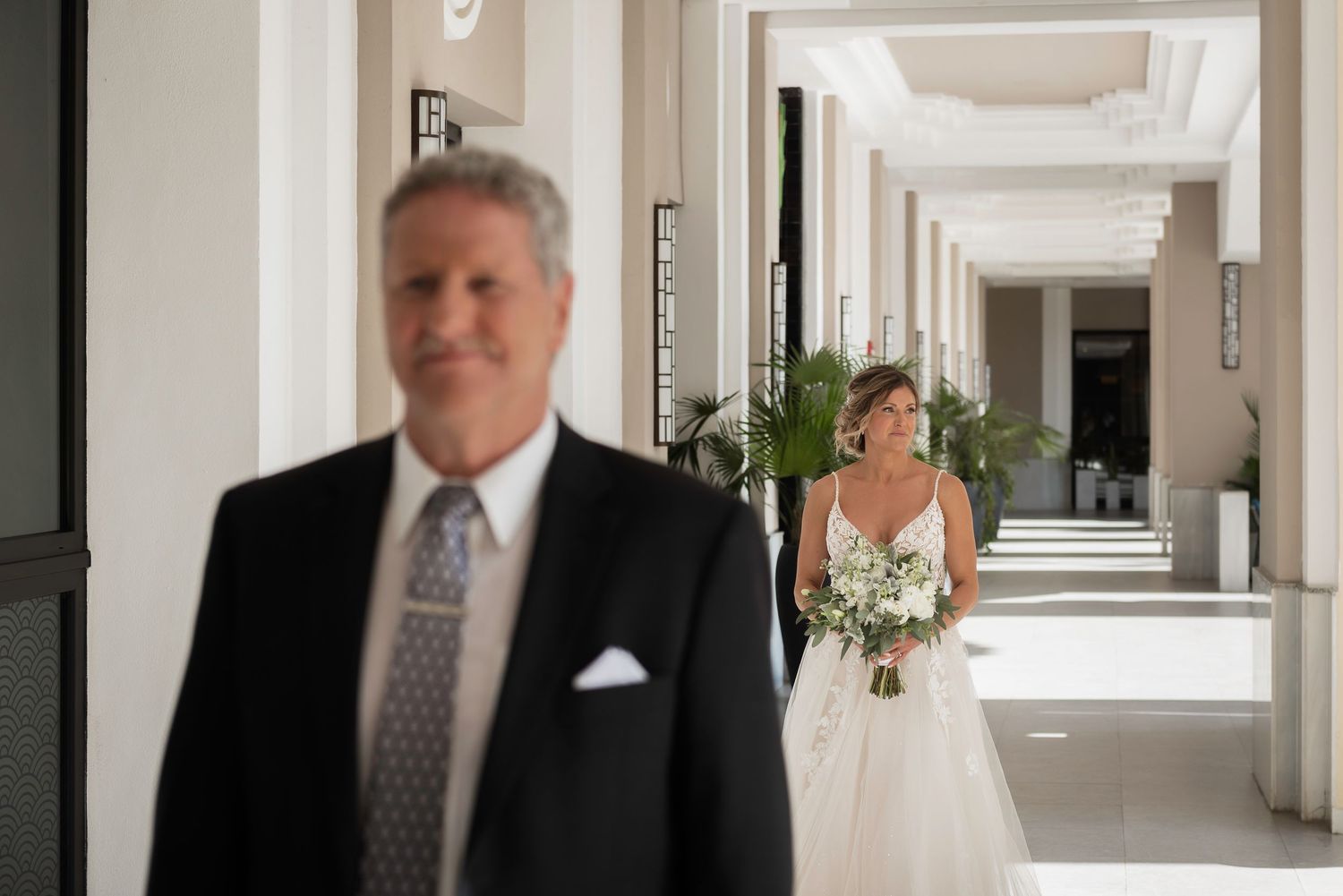First look moment between father and bride in elegant white hallway.