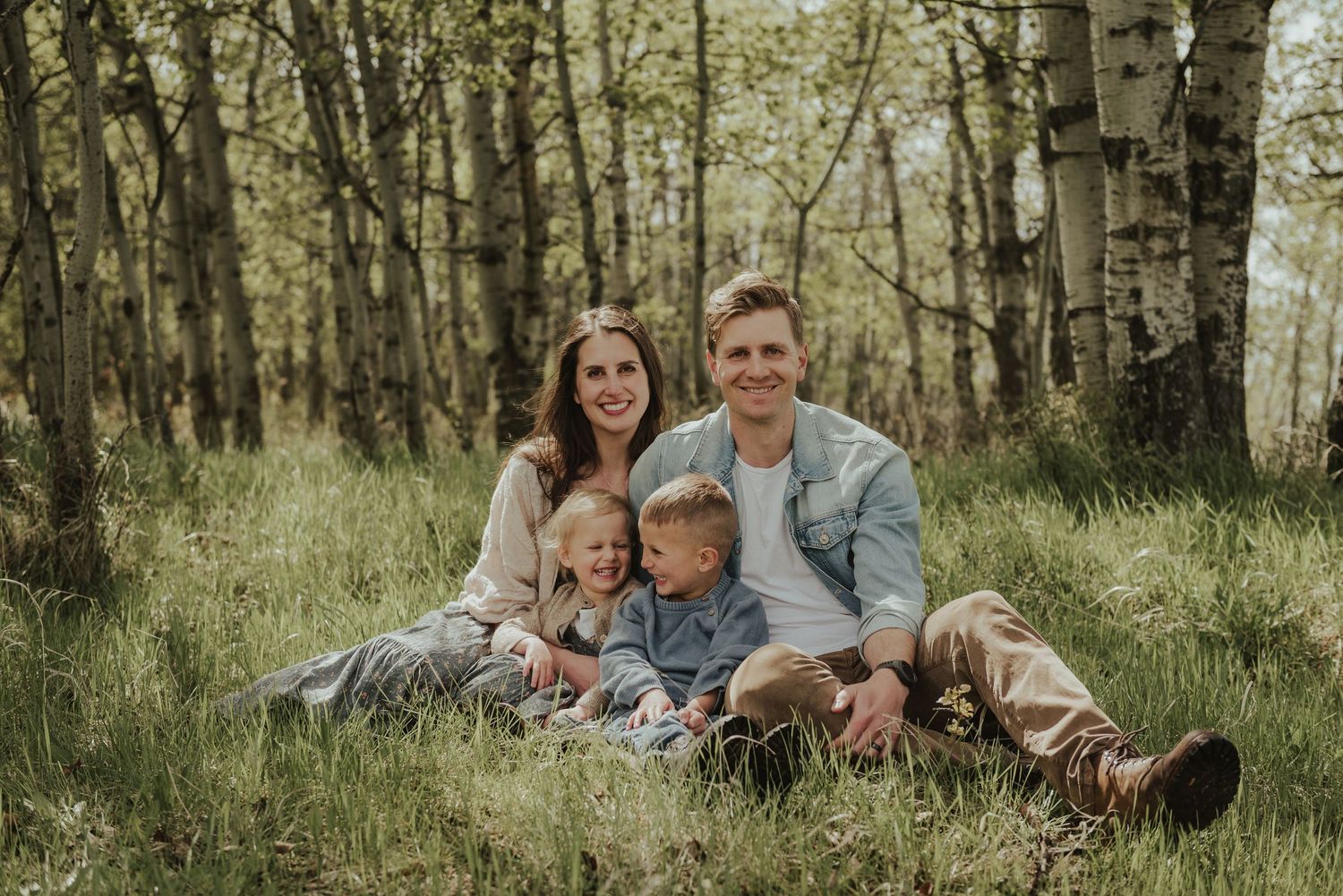 A family sits together on grass in a birch forest during a photo session.