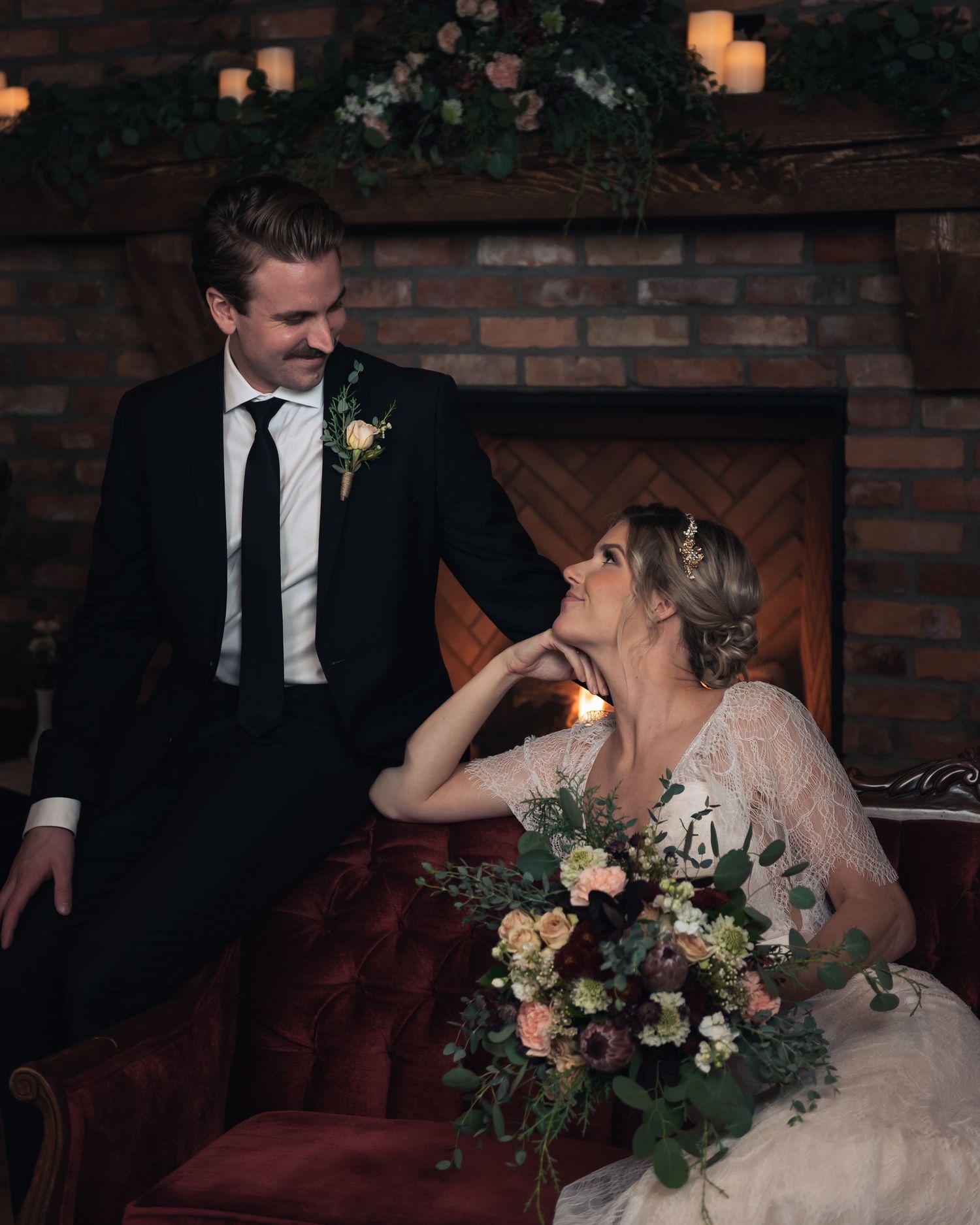 Couple shares intimate moment by brick fireplace decorated with candles and floral arrangements.