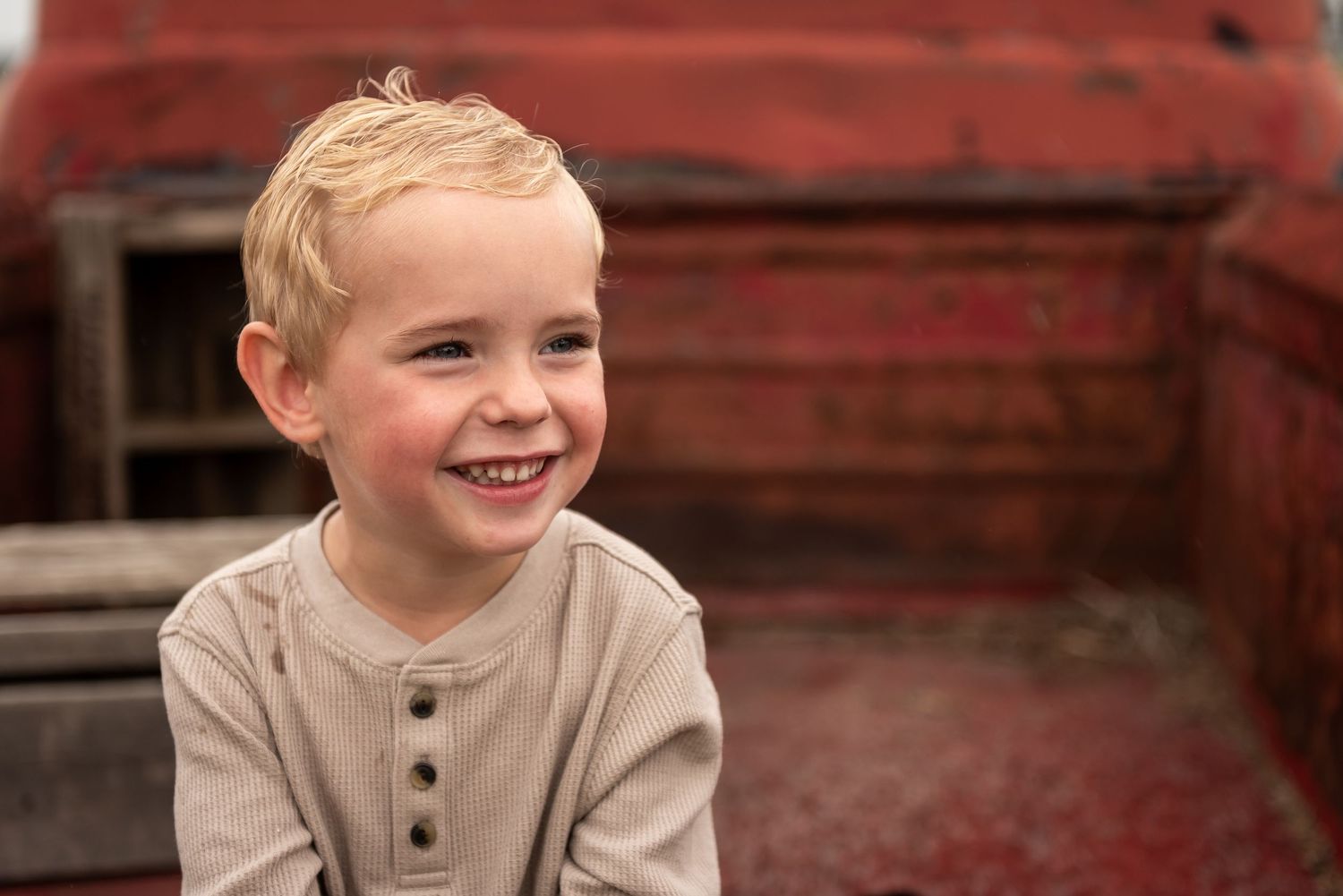 Young child smiling brightly against red rustic barn background.