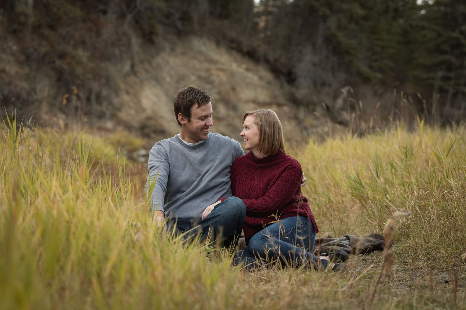 A couple sits together in tall autumn grass during a romantic outdoor photoshoot.