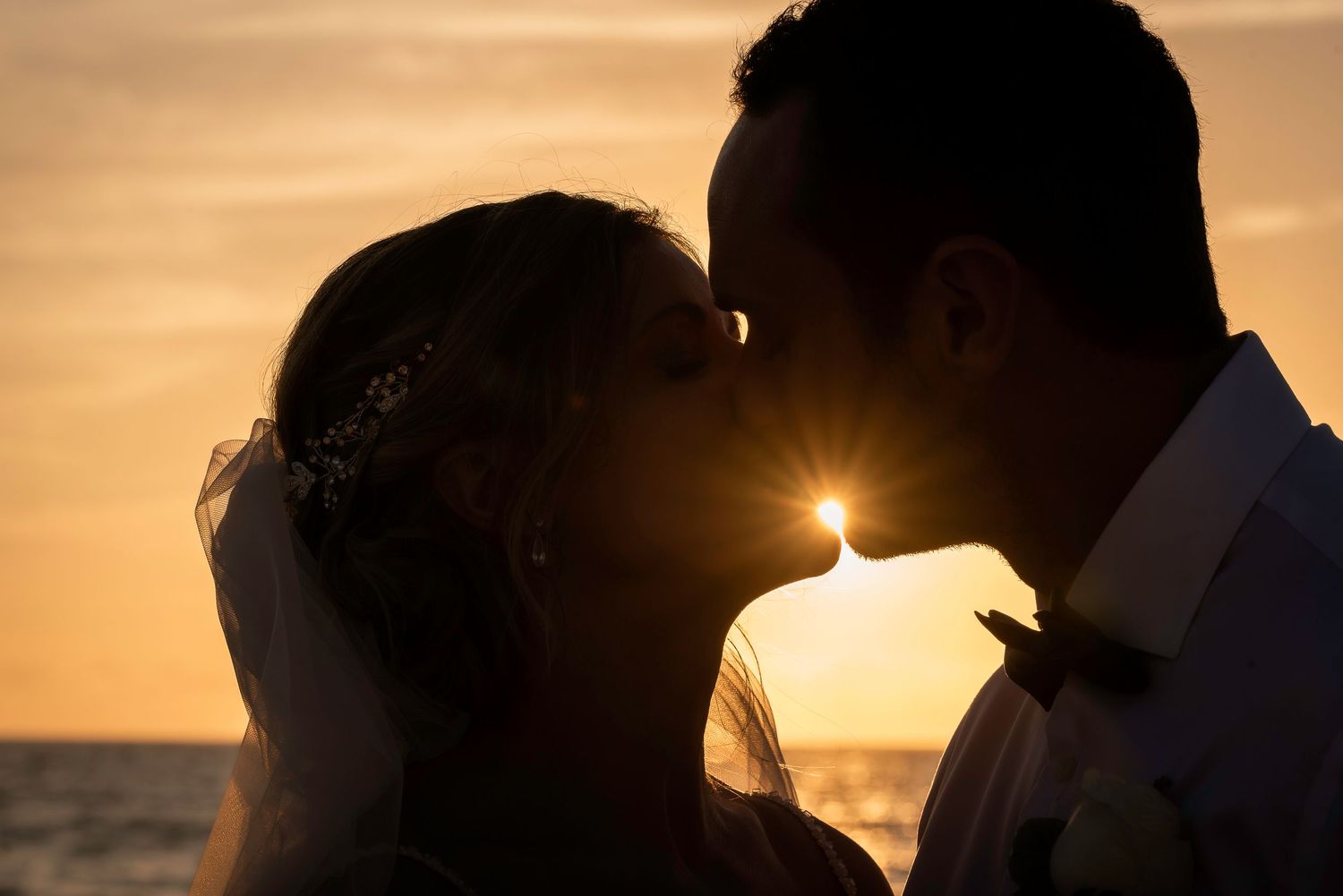 Silhouetted couple sharing an intimate moment against a golden sunset over the ocean.