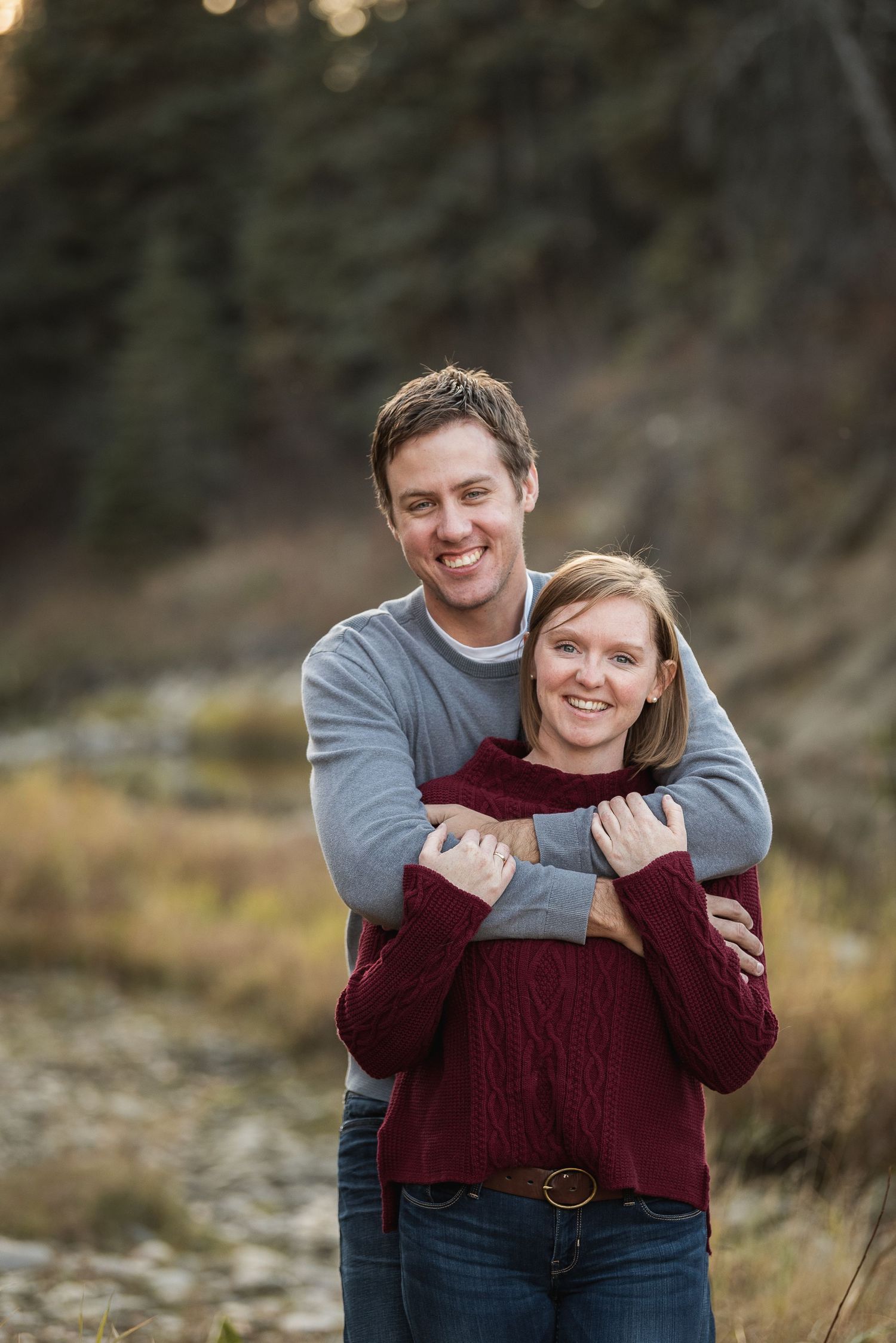 A couple embraces outdoors while wearing casual sweaters during an autumn photoshoot in nature.