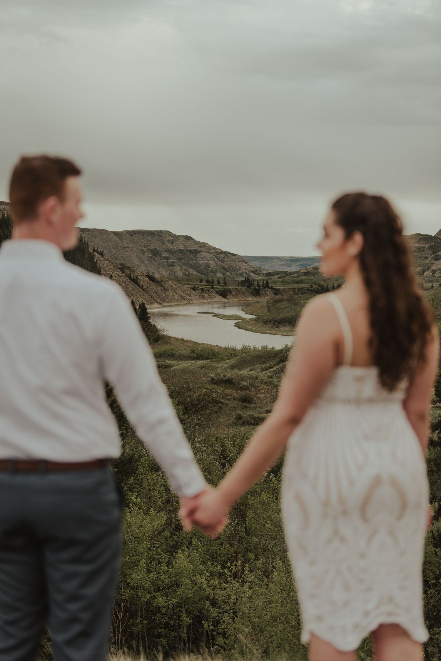 Couple enjoying scenic overlook of river valley while holding hands.