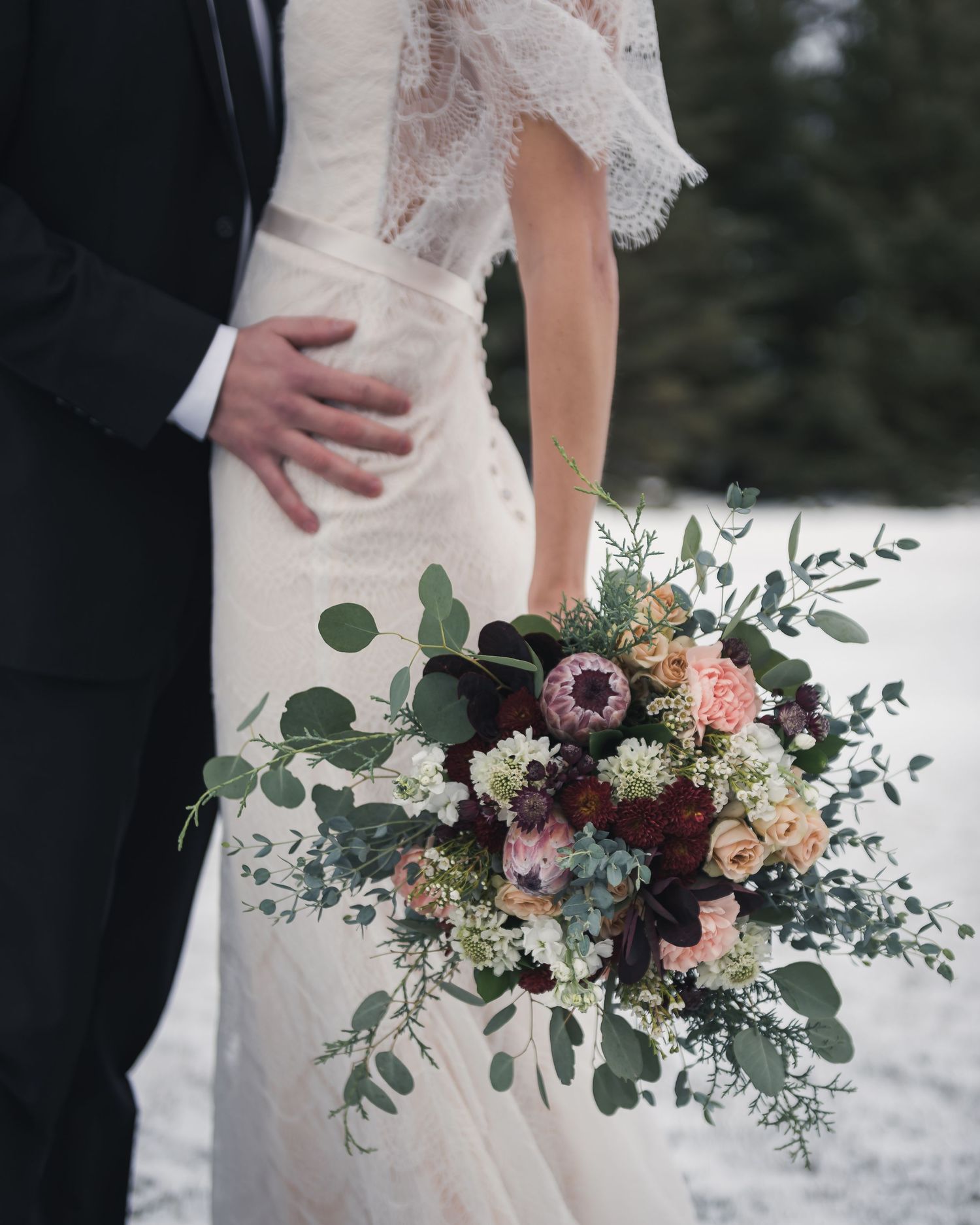 Close-up of bride holding elegant bouquet with burgundy and pink flowers and eucalyptus.