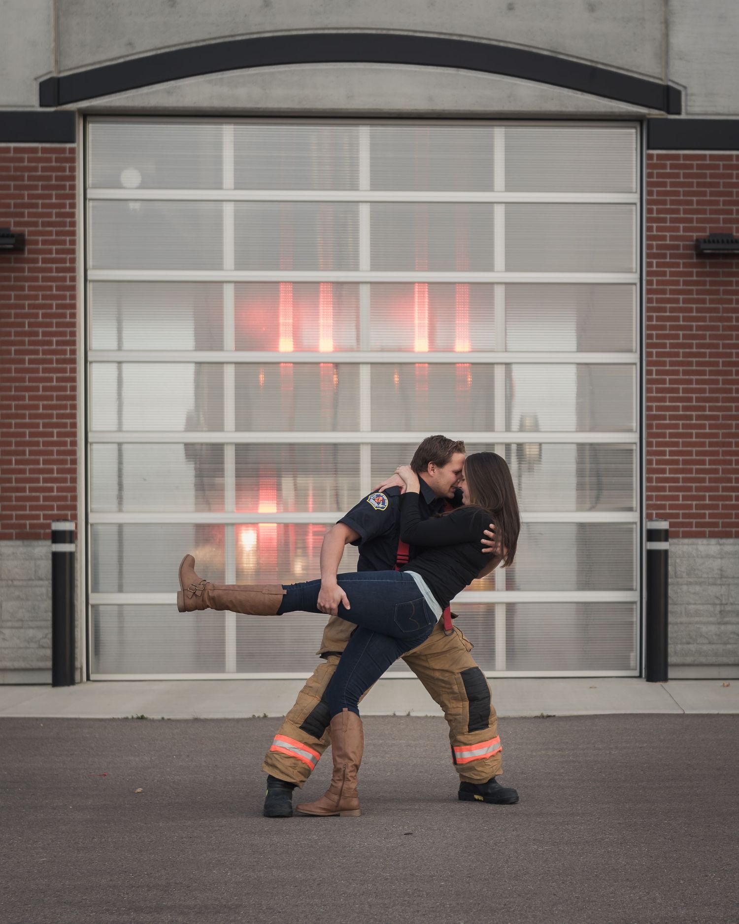 Romantic dip pose in front of a fire station garage door with dramatic red lighting.