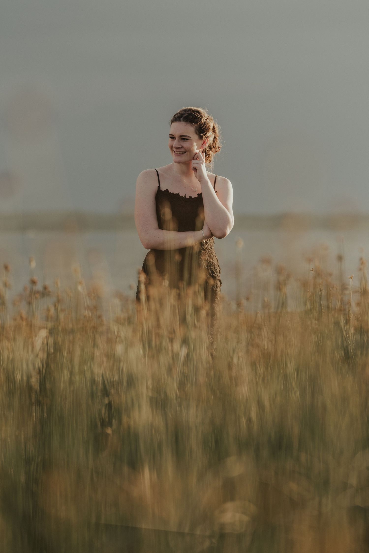 A person stands in a golden wheat field at sunset wearing a dark dress.