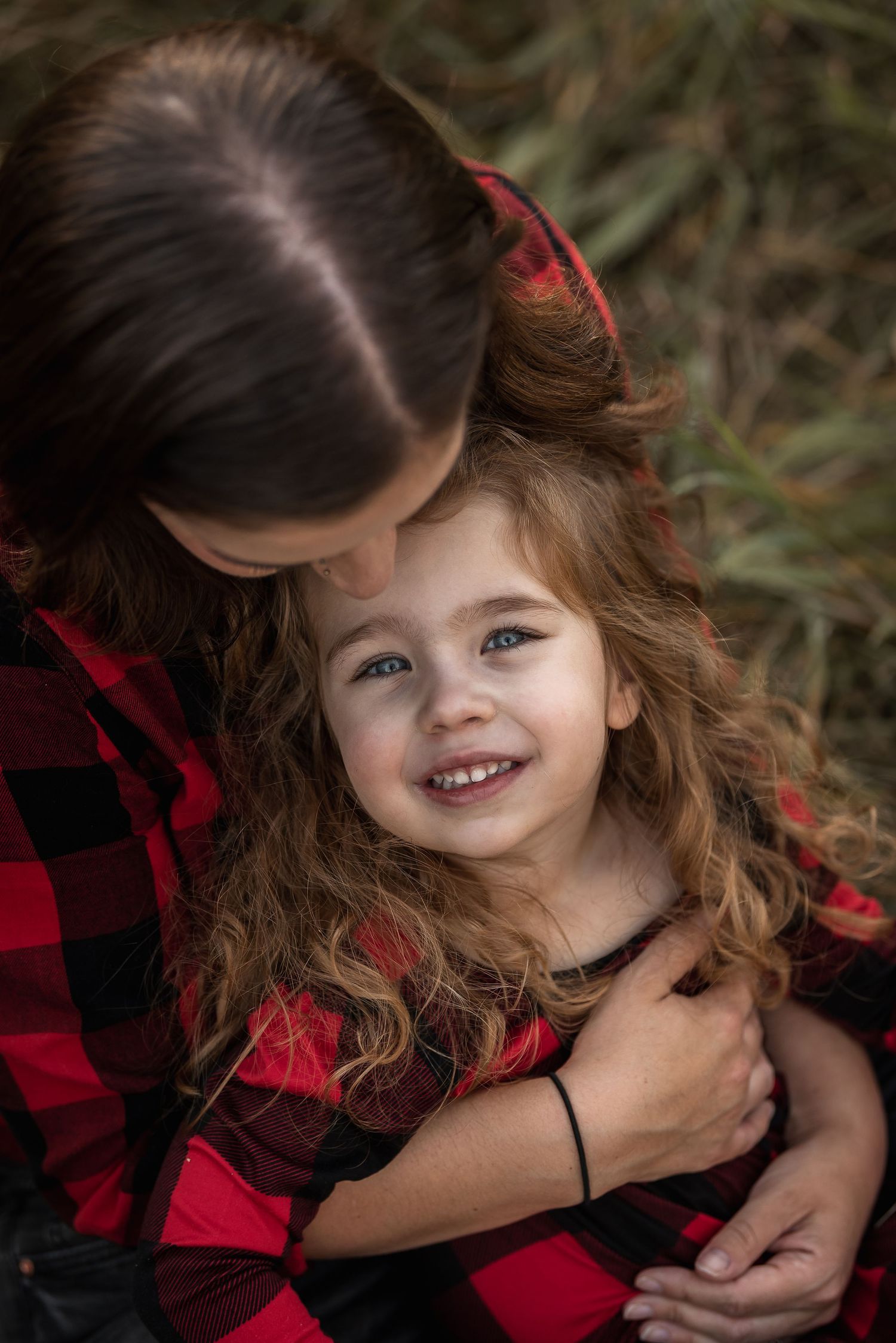 Tender moment between mother and daughter wearing buffalo plaid in autumn setting.