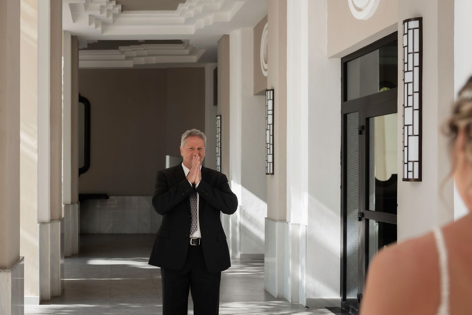 Emotional father reaction during first look with bride in bright hallway.