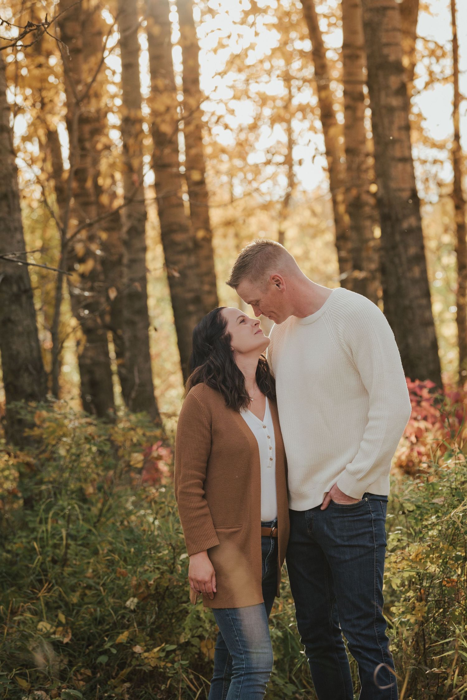 Autumnal forest engagement photo with couple in cozy sweaters among golden birch trees.