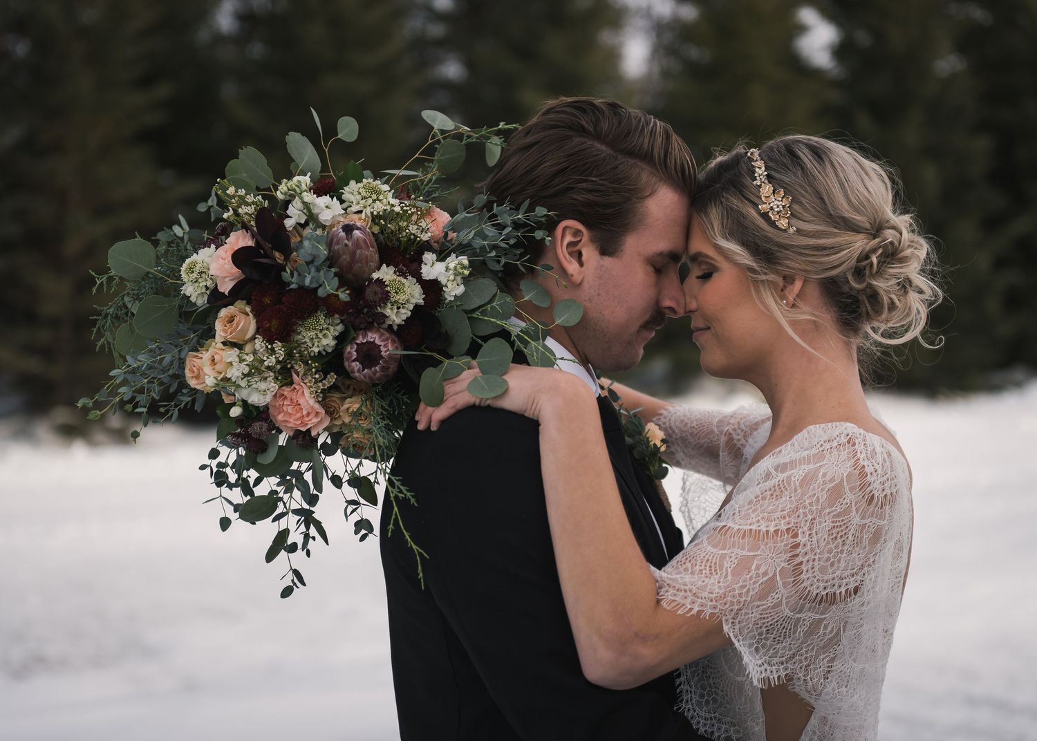 Couple embraces in snowy setting with lush winter wedding bouquet.