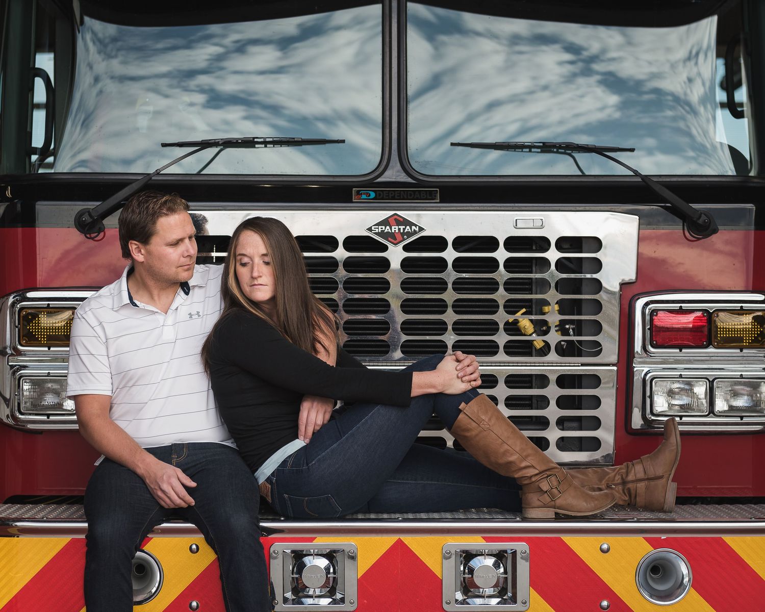 Couple poses romantically on the front of a red fire truck during an engagement photoshoot.