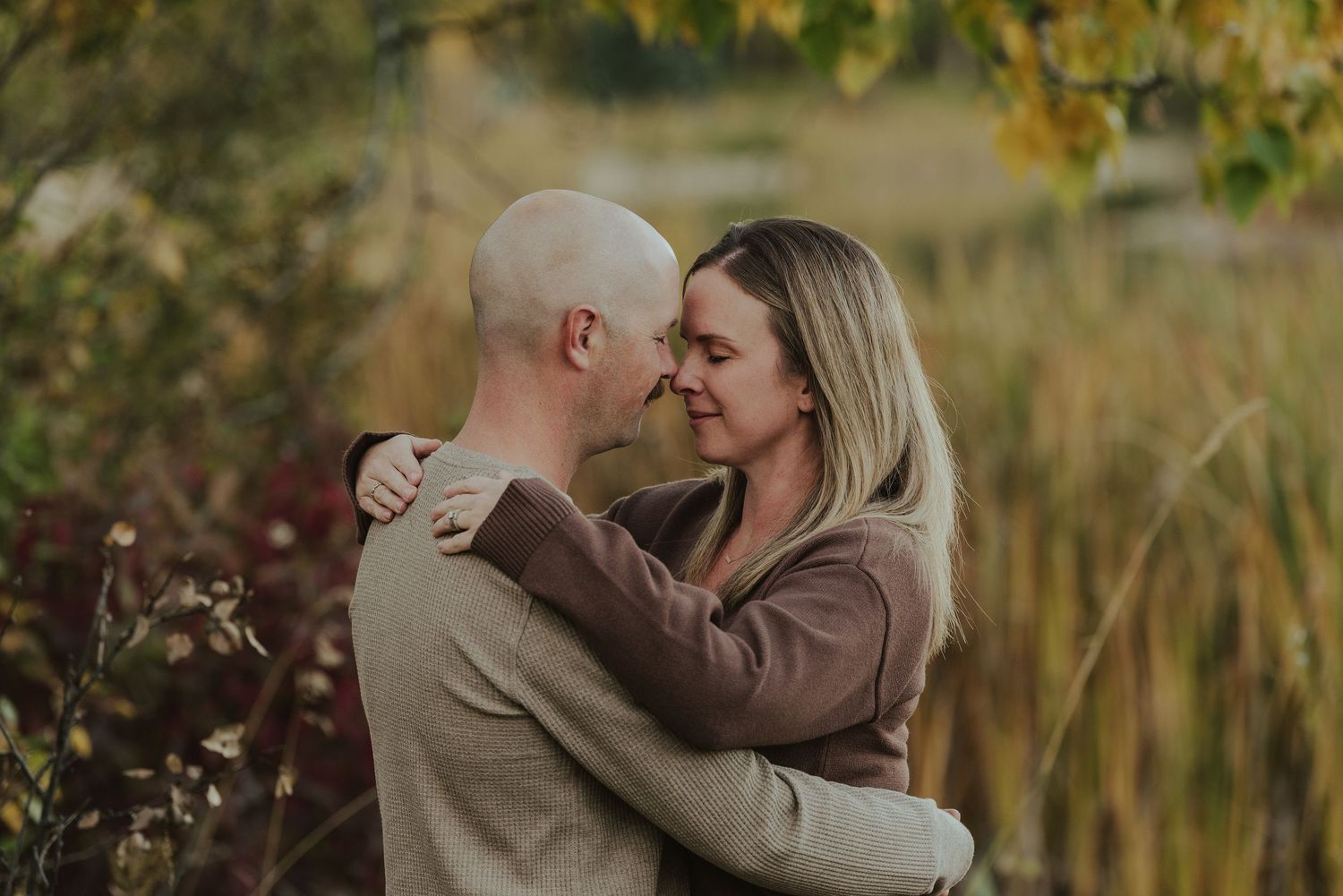 Tender embrace between couple in warm autumn clothing against natural fall backdrop.