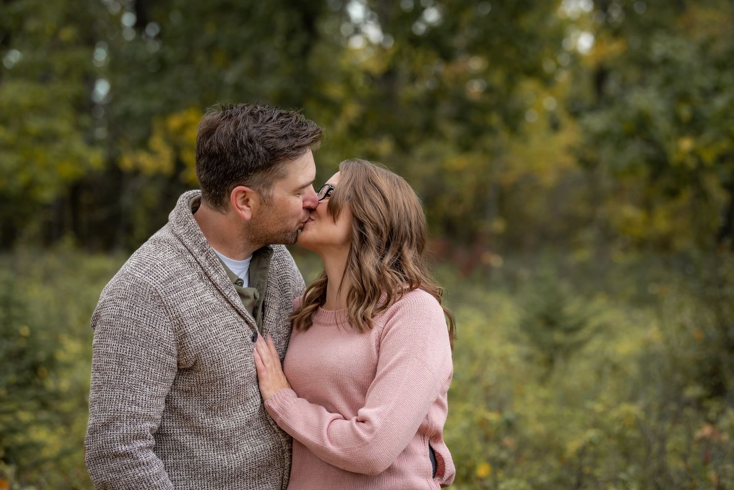 Romantic autumn outdoor portrait of a couple embracing in cozy sweaters among fall foliage.