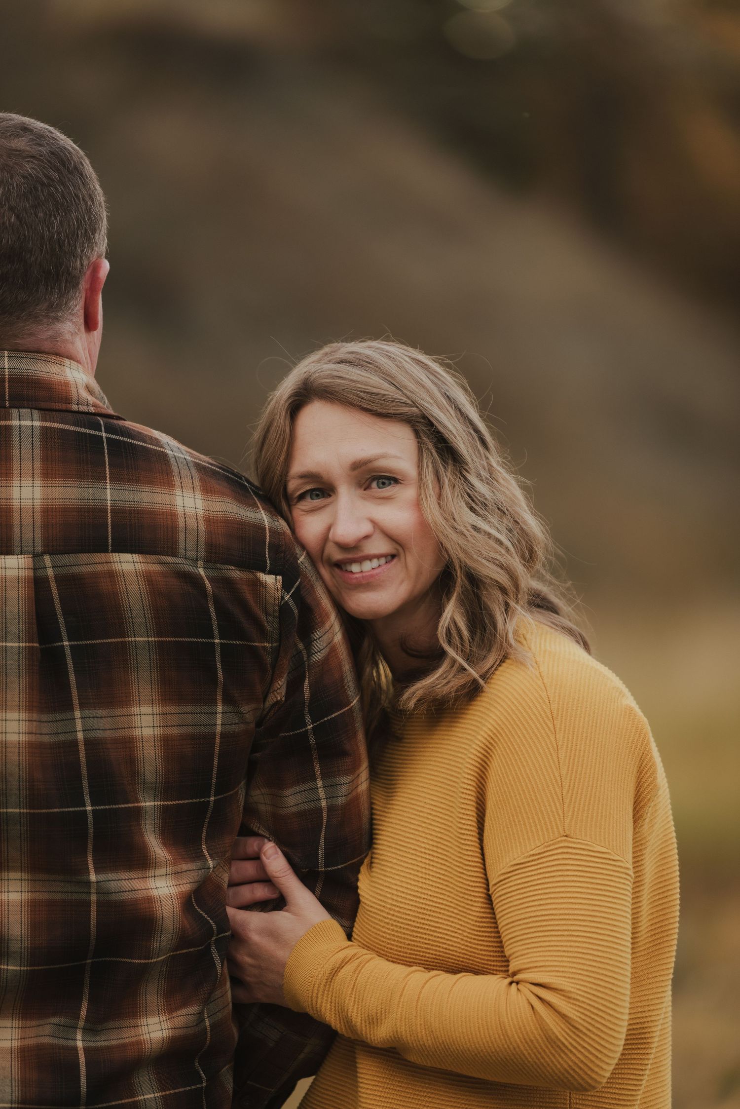 A couple shares a romantic moment outdoors wearing autumn colors during golden hour.