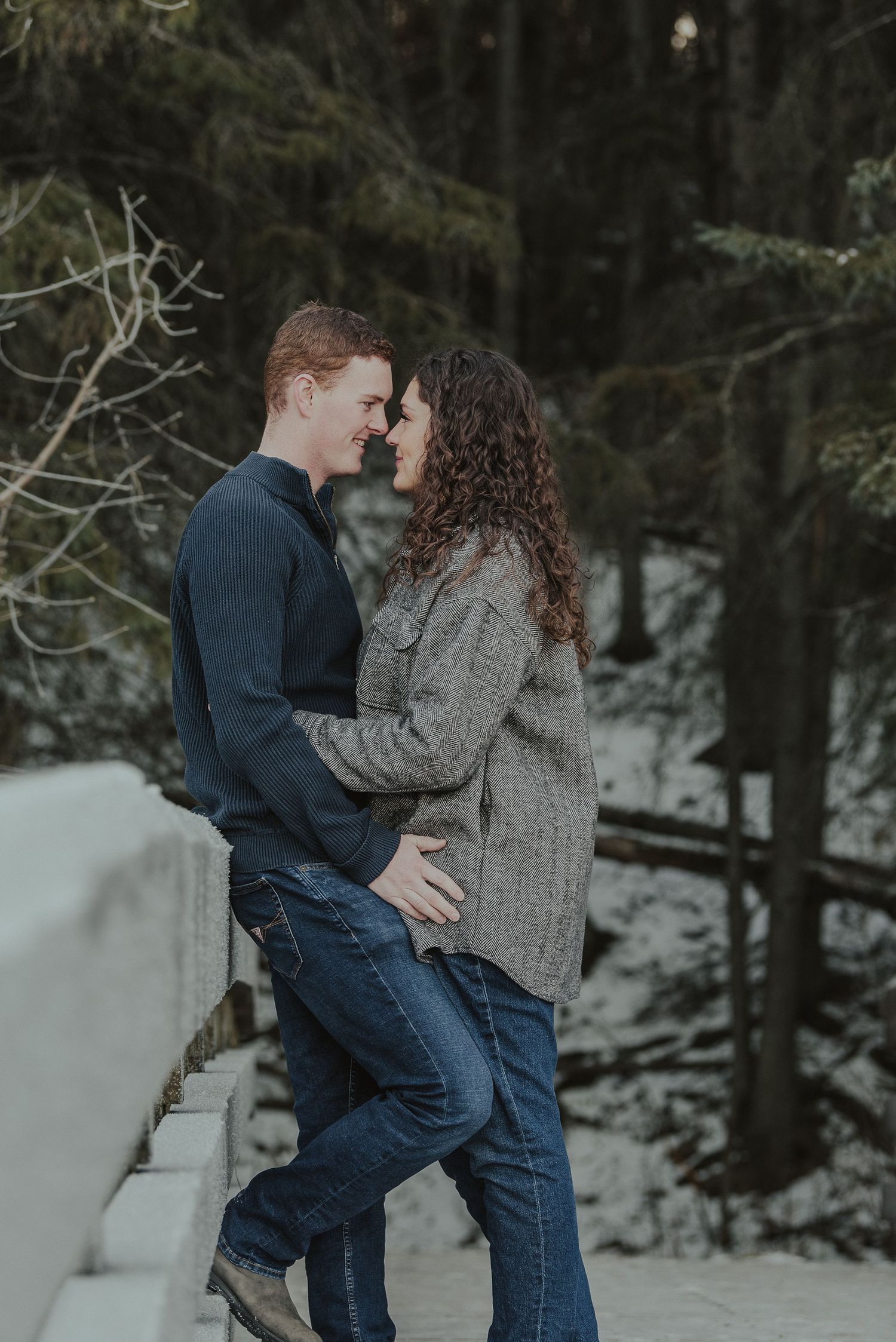 Winter engagement photo of couple in warm sweaters sharing an intimate moment in snowy setting.