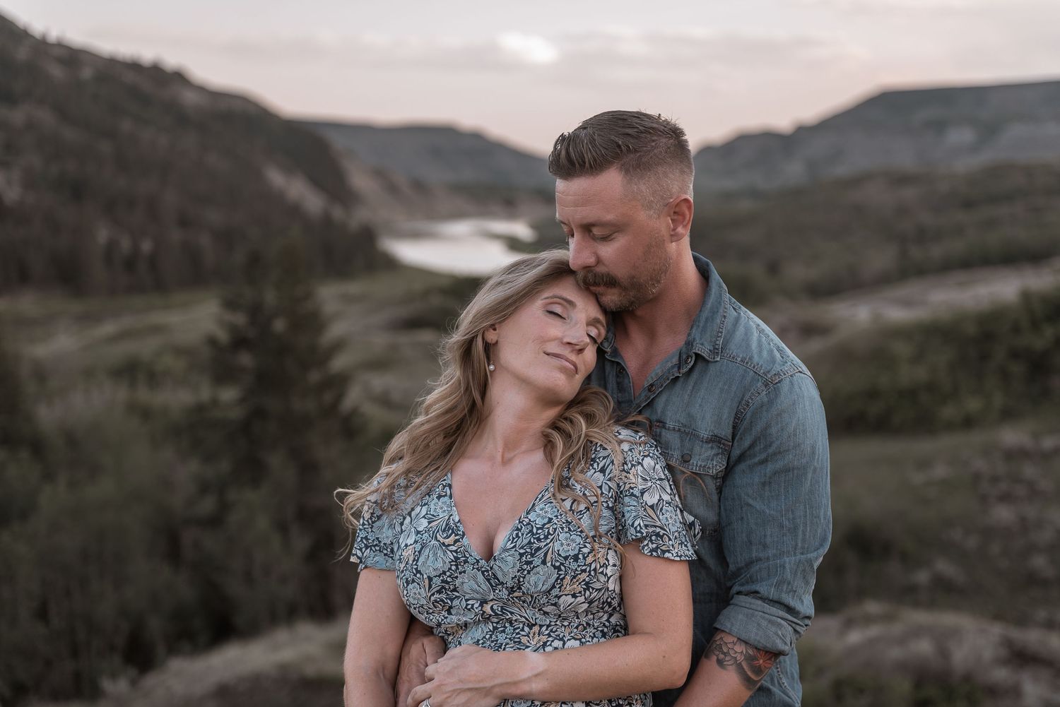 Couple embraces intimately against scenic mountain backdrop at dusk in a romantic outdoor setting.