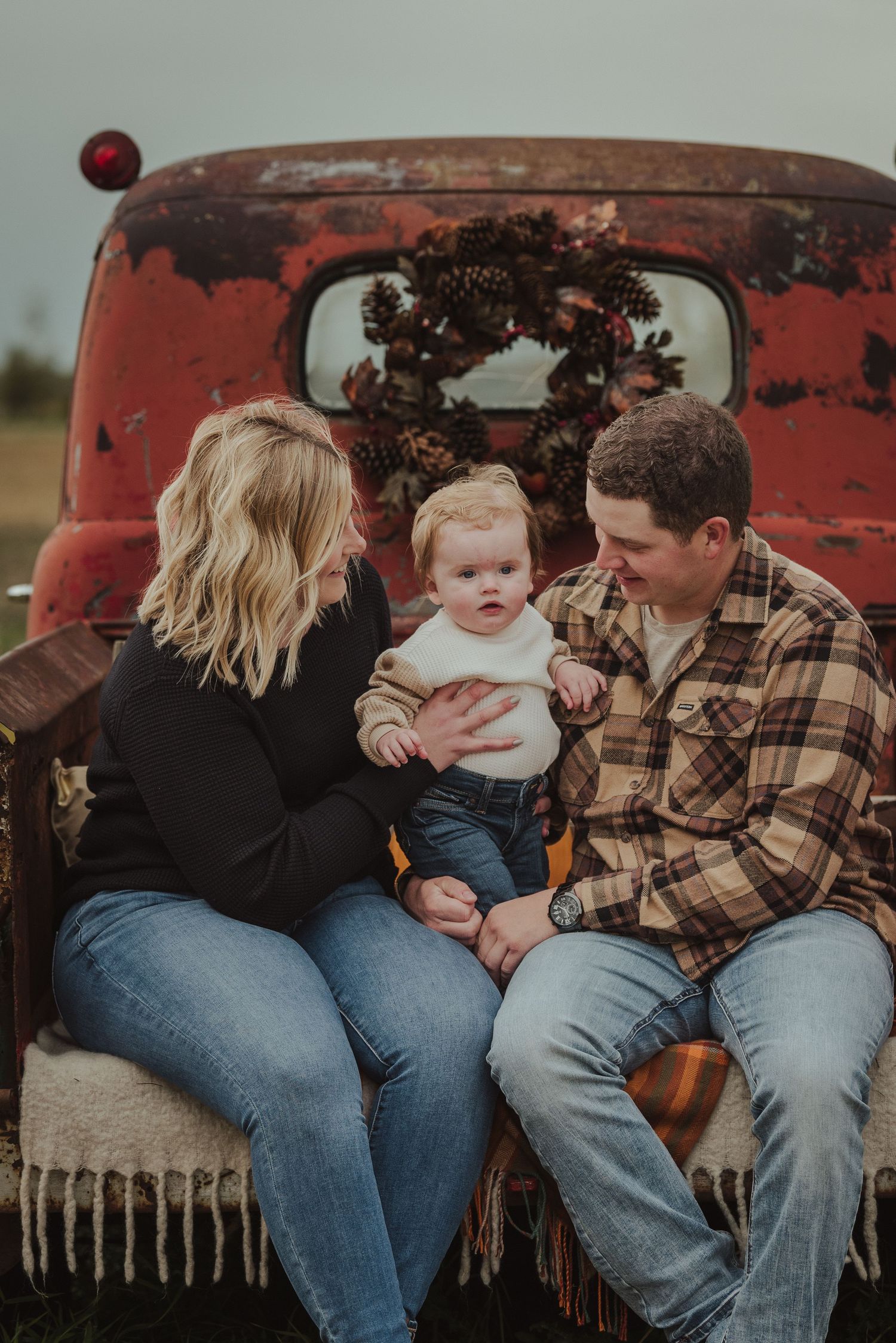 Family sitting on vintage red truck tailgate with holiday wreath decoration.