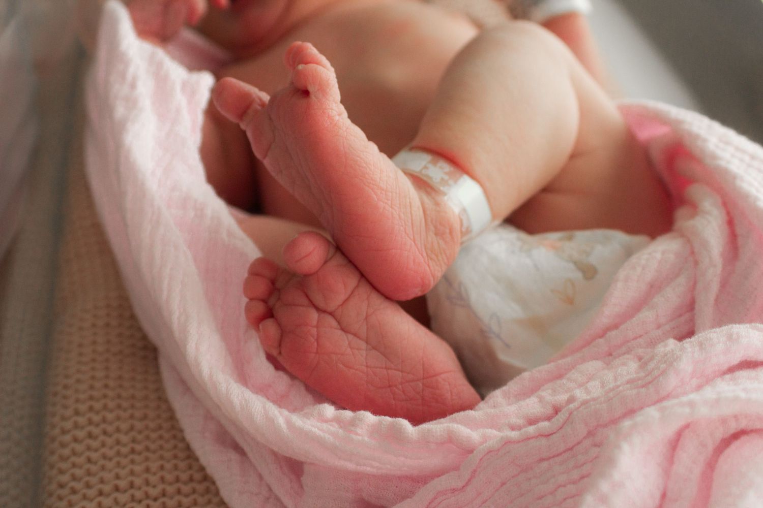 Close-up of newborn baby's tiny feet wrapped in pink blanket.