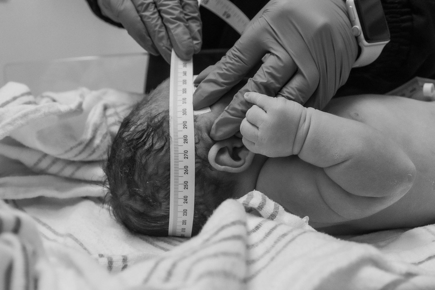Healthcare provider measuring newborn baby's head circumference with measuring tape.