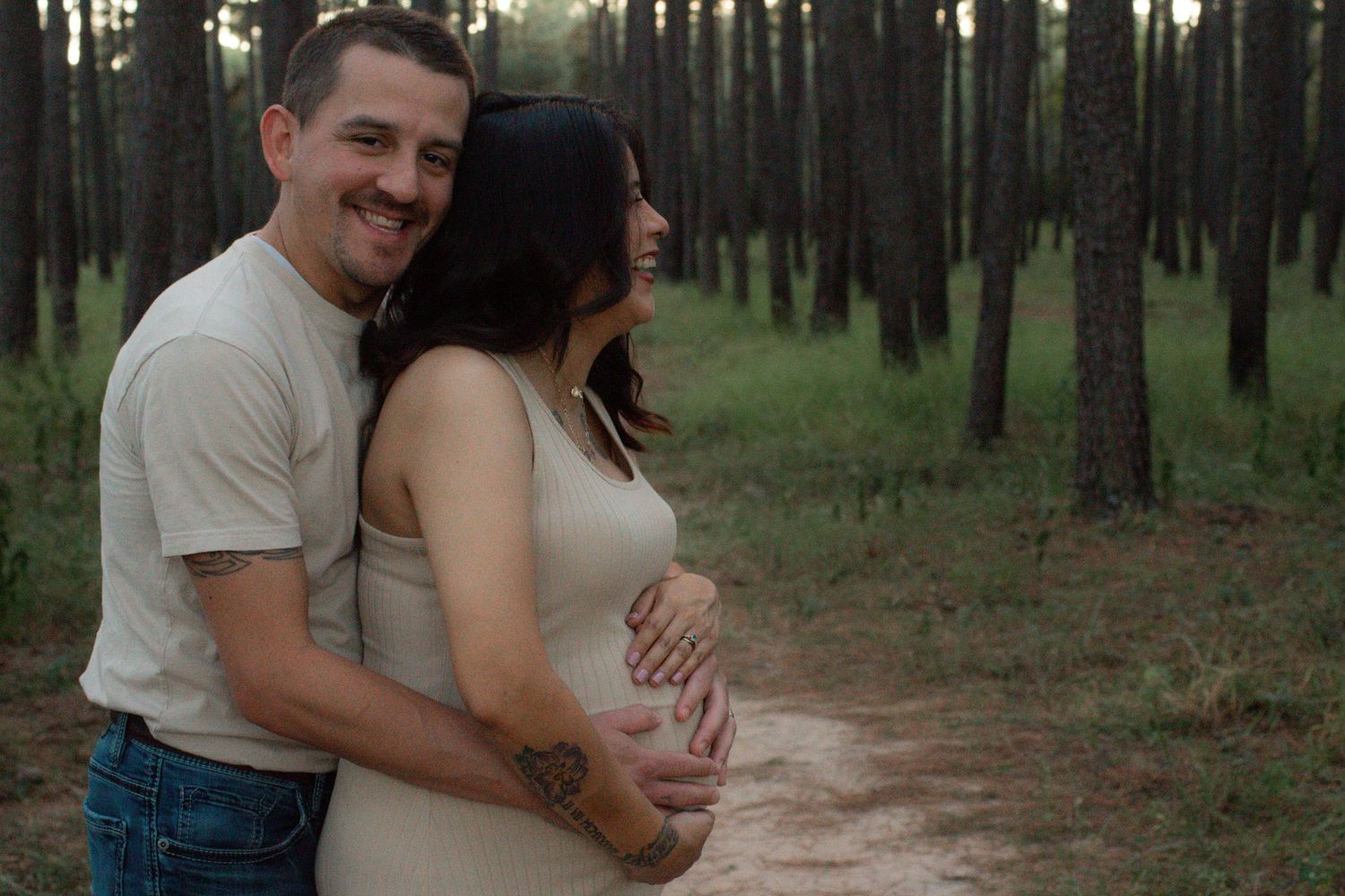 Intimate maternity moment captured between couple in wooded setting.