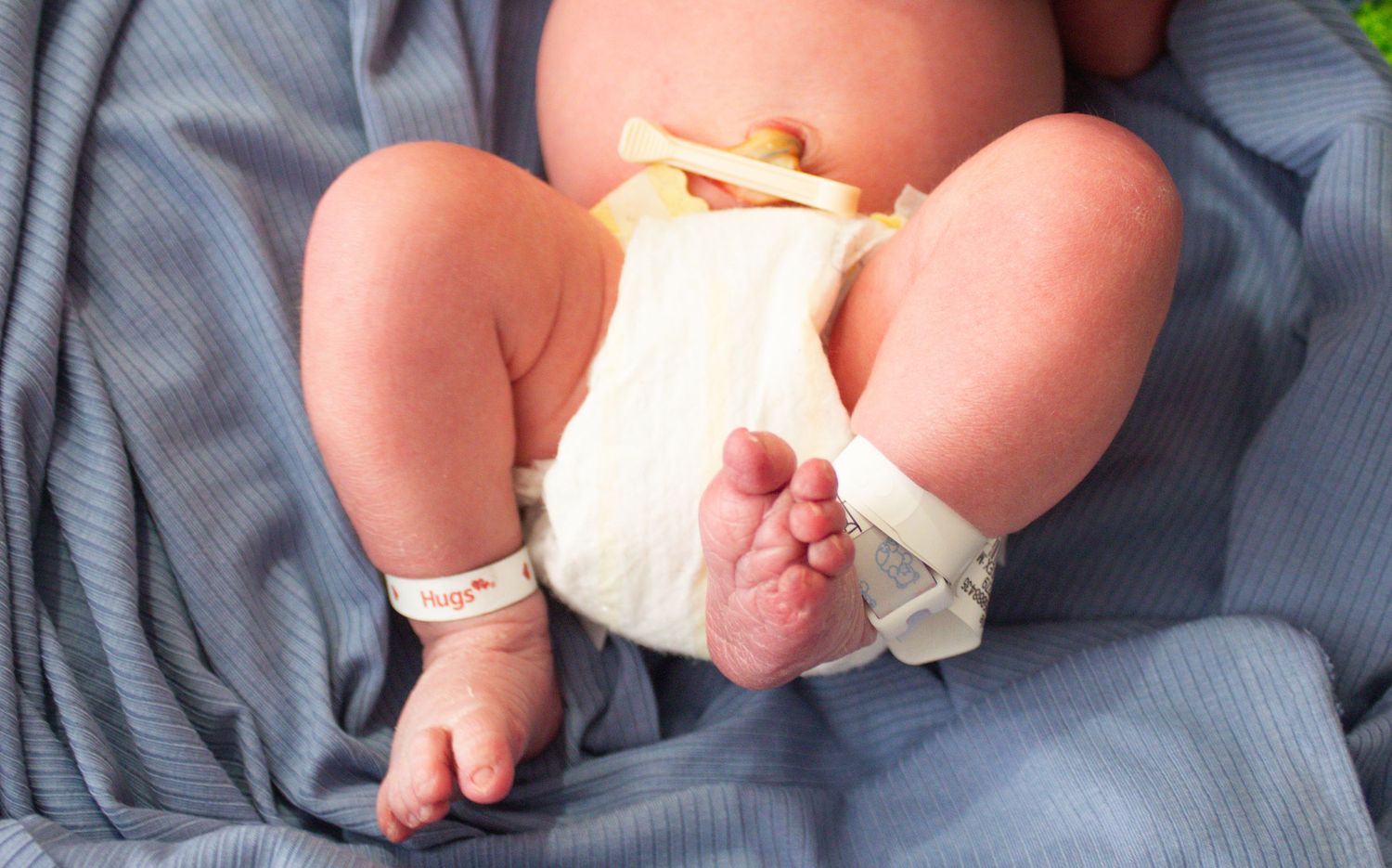 Tiny baby feet and legs in white diaper on blue fabric.