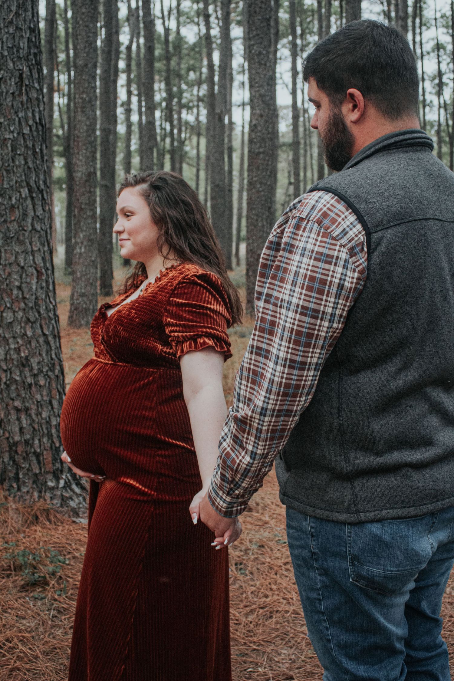 Expectant couple share intimate moment in pine forest setting.