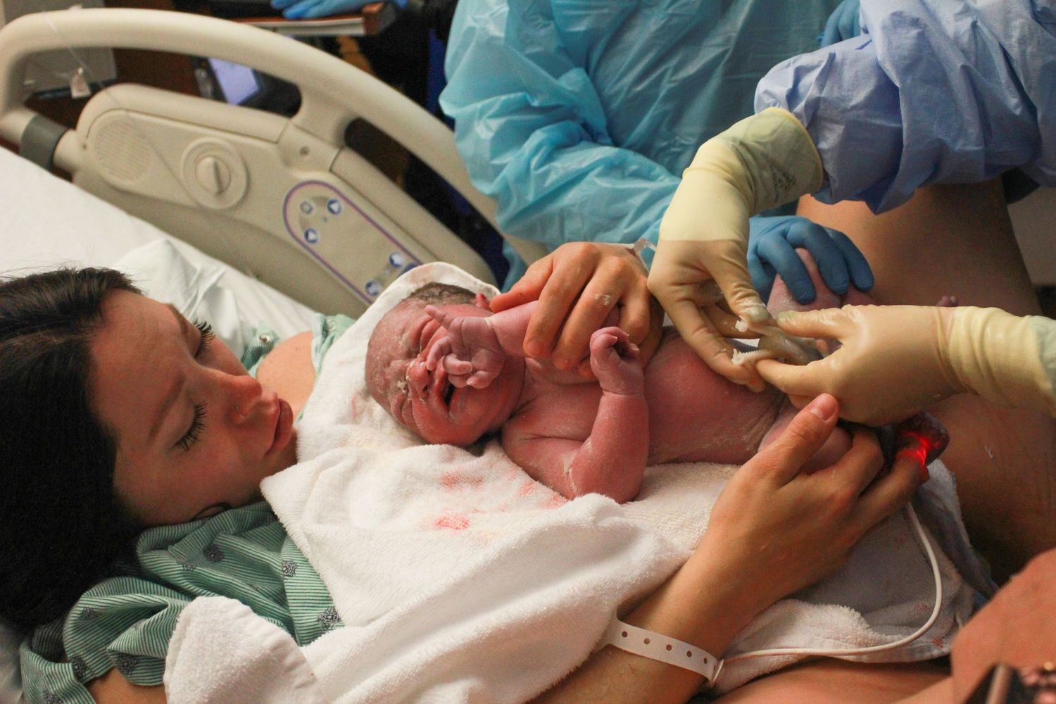 A newborn baby taking their first breath during an emotional delivery room moment.
